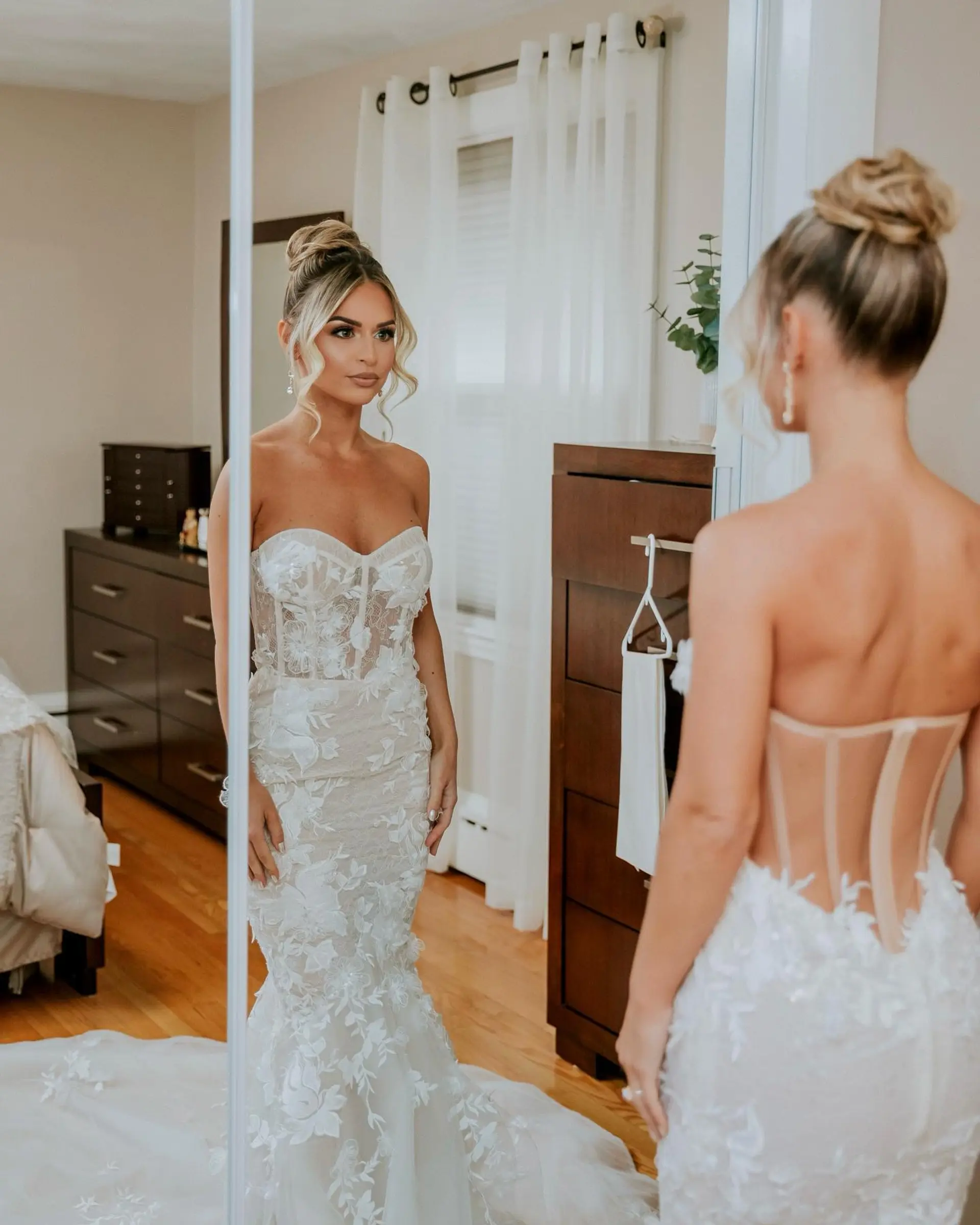 A glamorous bridal high bun updo featuring soft, wavy face-framing tendrils and dimensional blonde coloring. 1