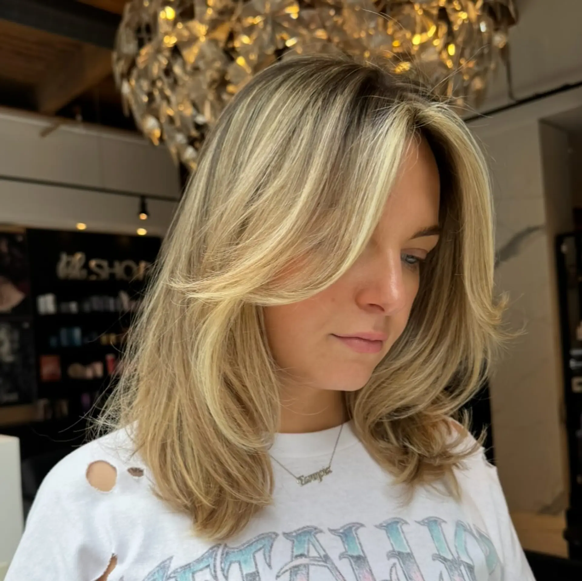 Medium-length layered haircut with face-framing curtain bangs and multi-dimensional blonde highlights, styled in a polished, voluminous blowout. 1