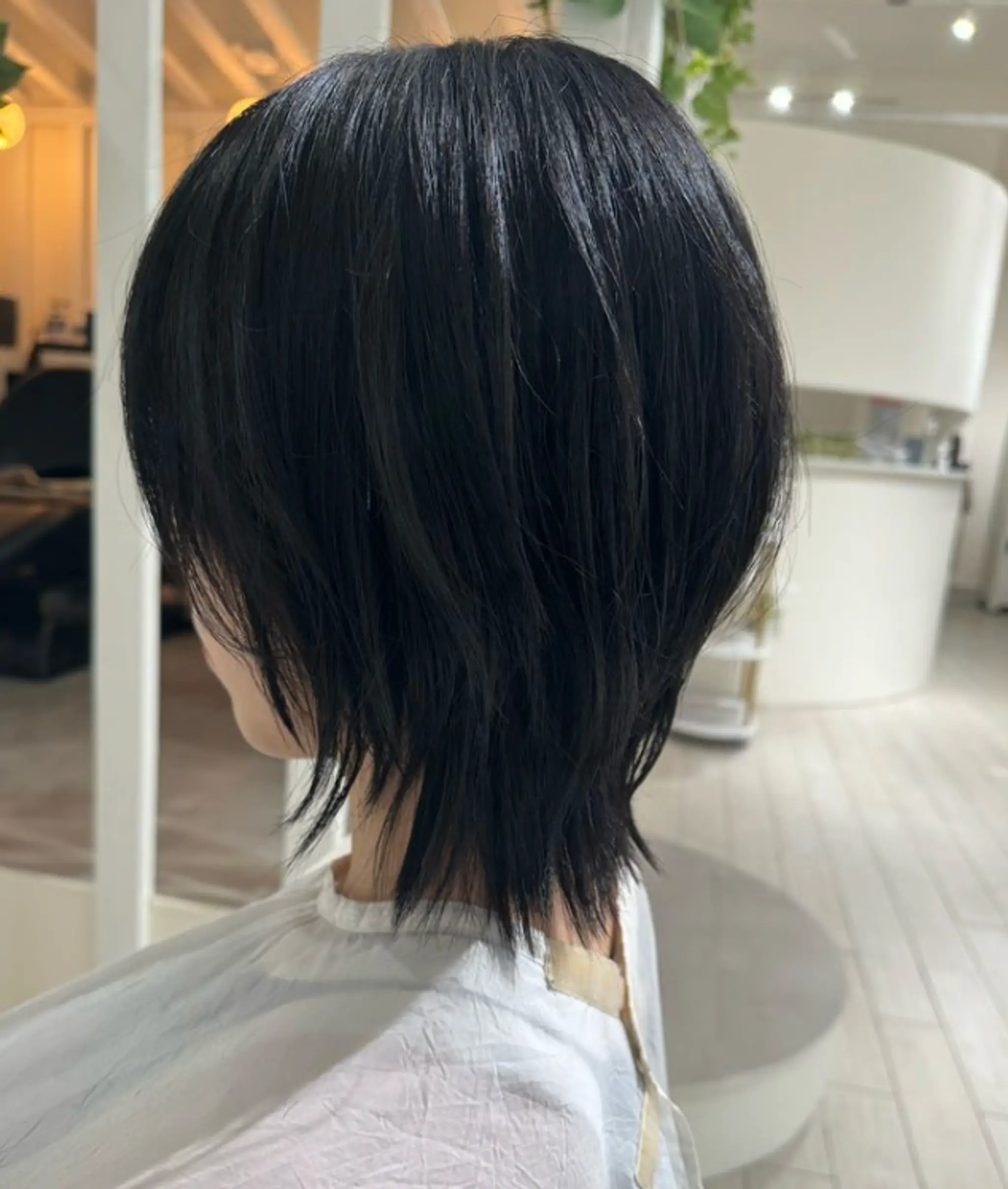 A medium-length, wavy hairstyle with layers, textured ends, and side-swept bangs in a shiny black color.

