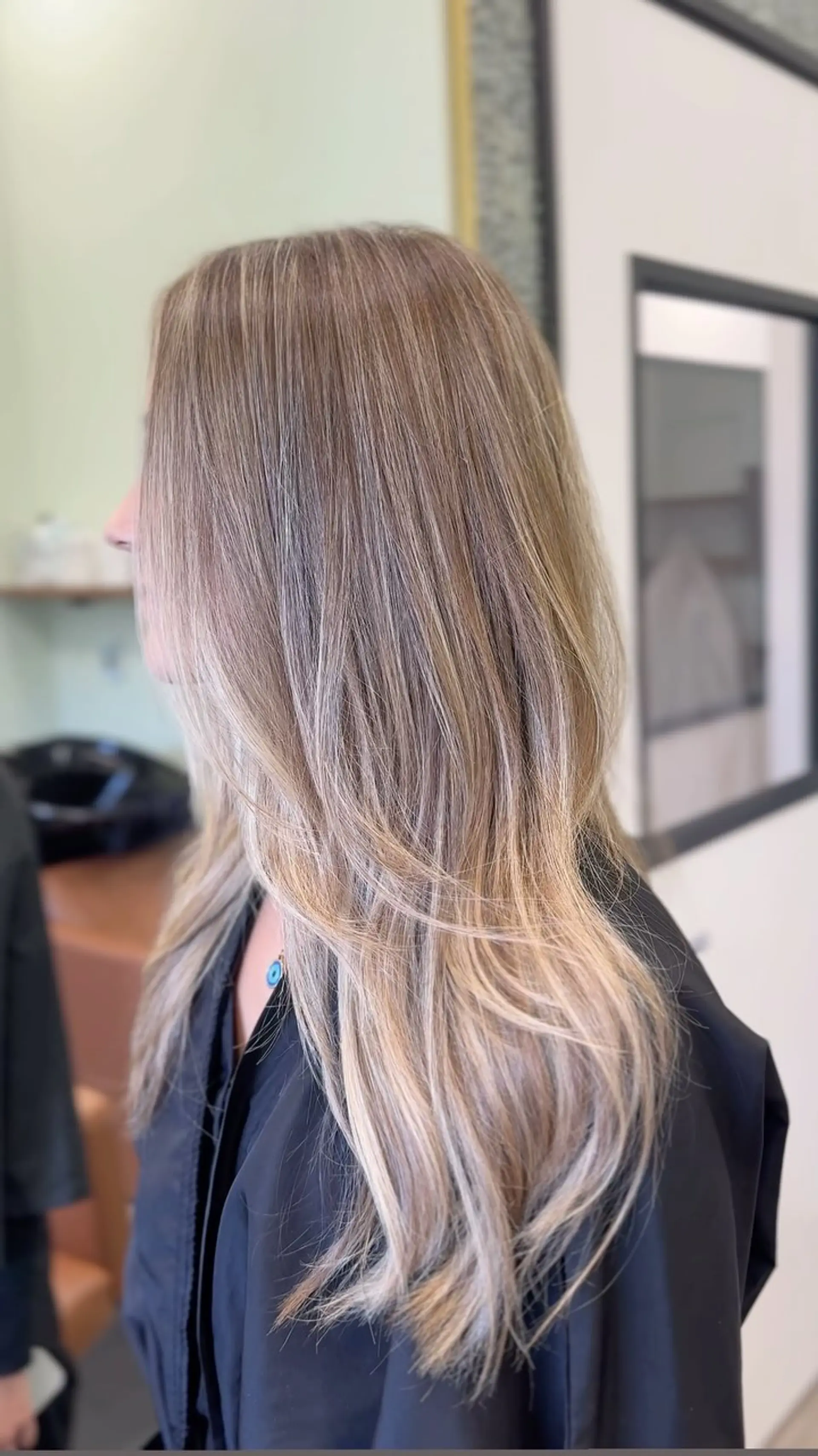Long layered hair featuring seamlessly blended ash and beige blonde balayage highlights over a soft light brown base, styled with smooth movement and flipped ends. 1
