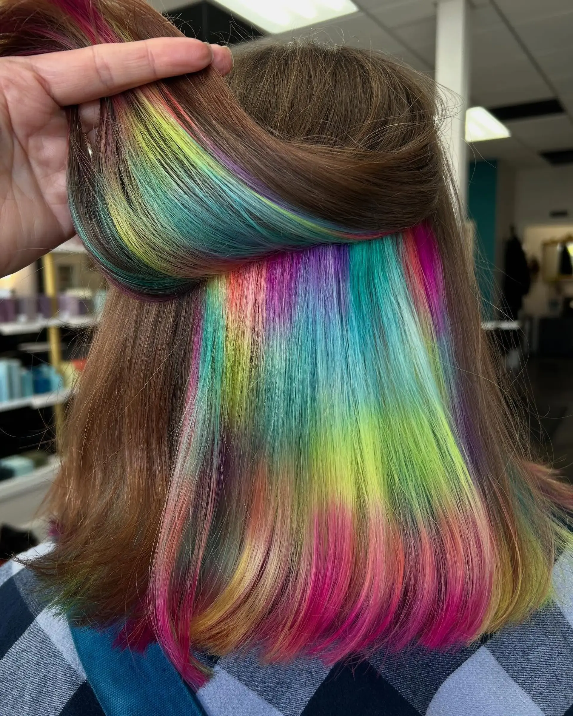 A medium-length straight haircut with natural light brown outer hair lifted to reveal an intricate holographic underlayer with vivid shades of pink, yellow, blue, and purple. 1