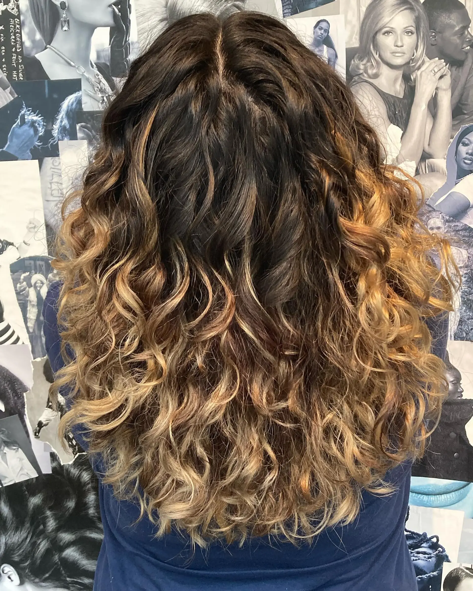 Long naturally textured or styled curls featuring a seamless blend from dark brown roots into warm caramel and honey blonde foiliage highlights. 1