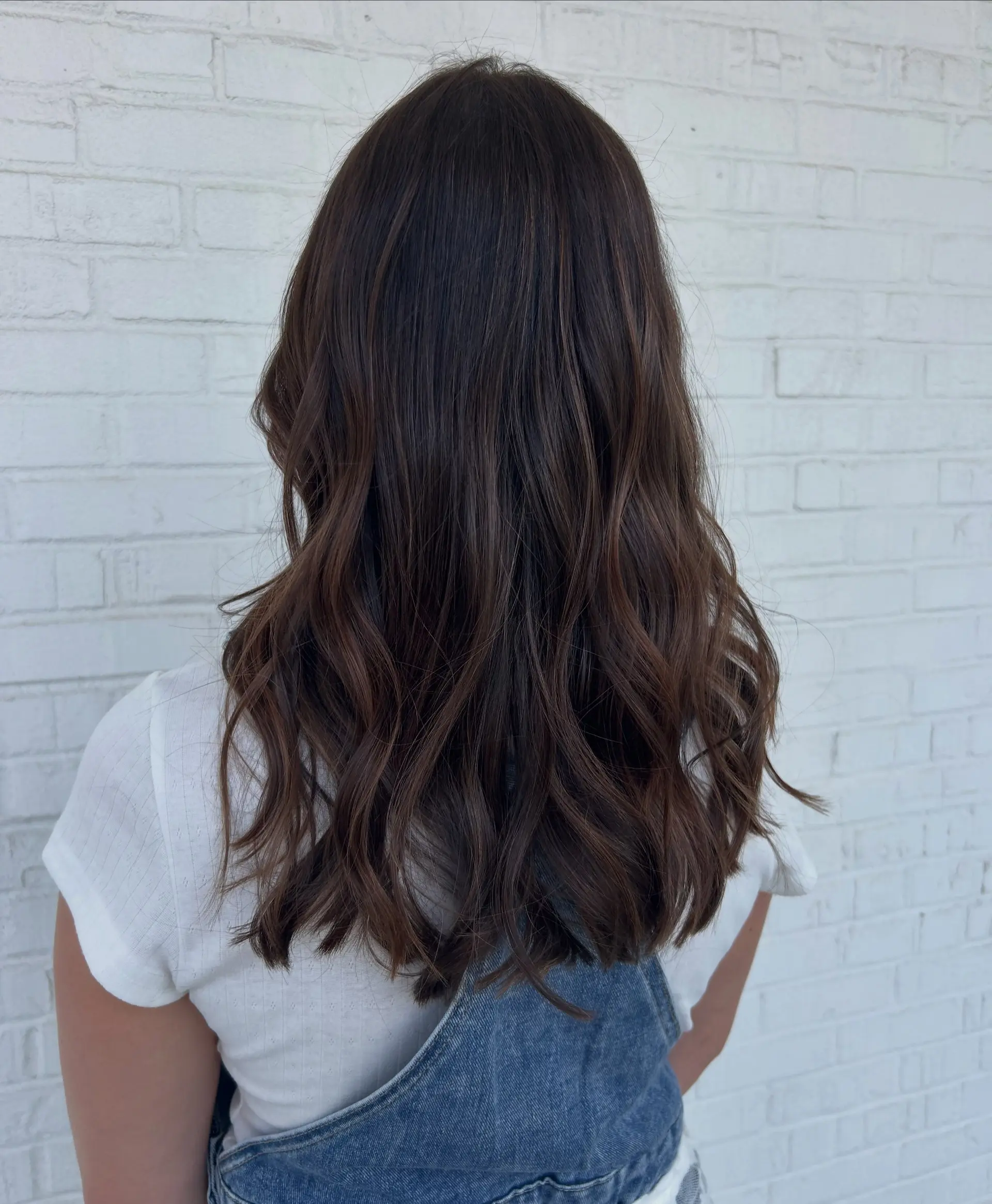 Long, rich dark brown hair enhanced with subtle, lived-in chocolate balayage highlights and styled into loose, effortless waves. 1
