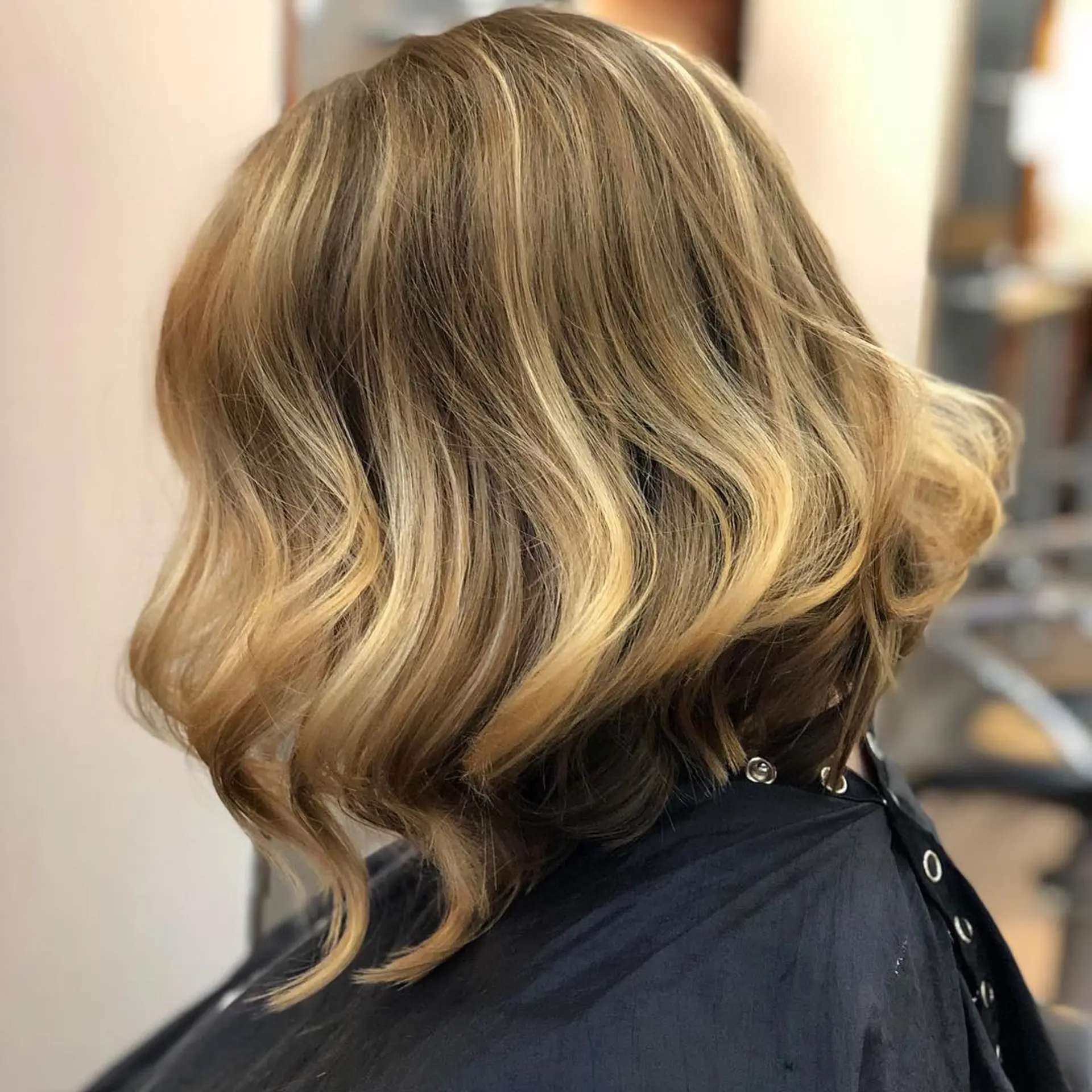An angled A-line bob cut styled with loose, dimensional waves and dirty blonde highlights. 1