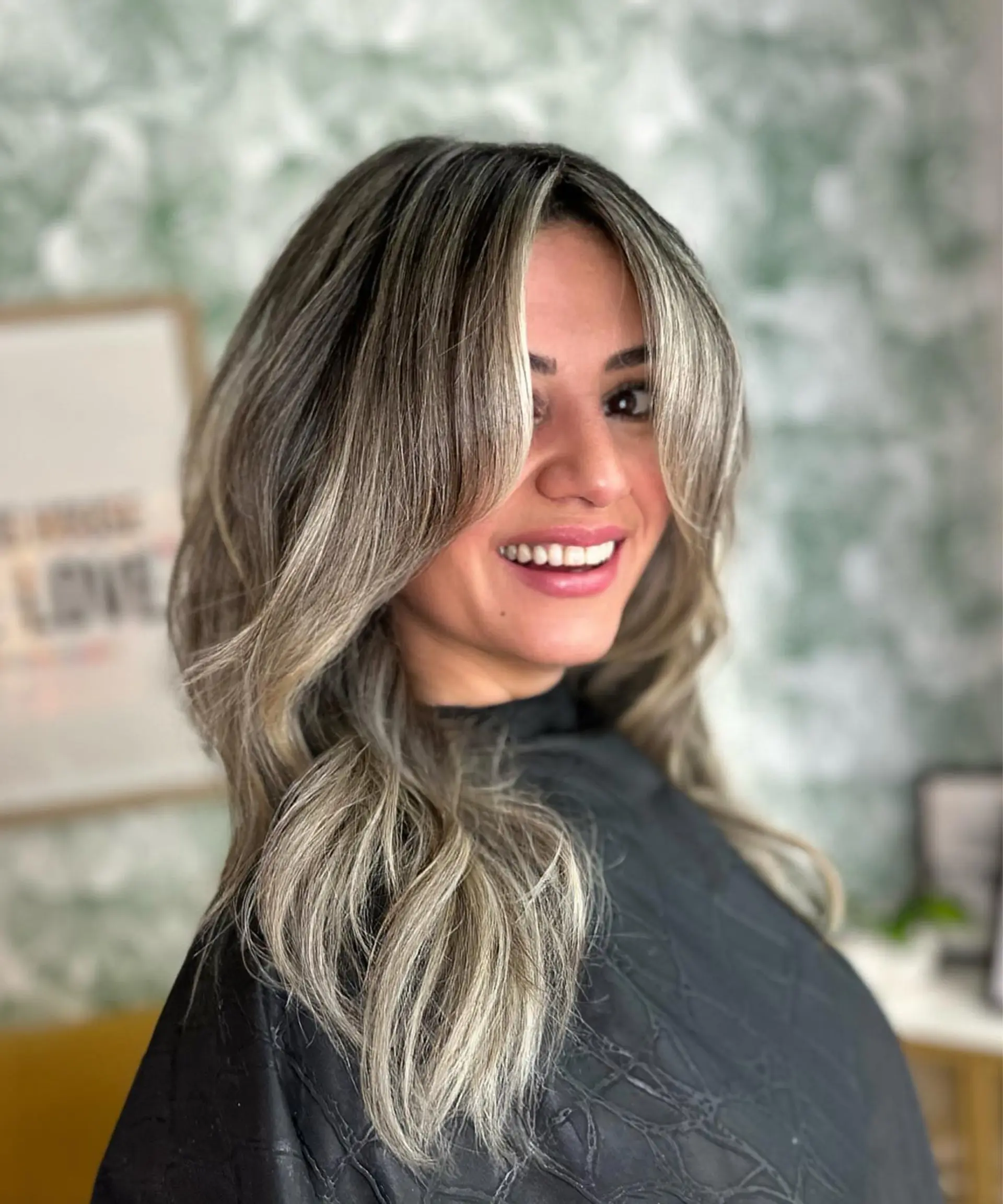 Long layered cut featuring face-framing curtain bangs and cool-toned ash blonde highlights styled into voluminous soft waves. 1