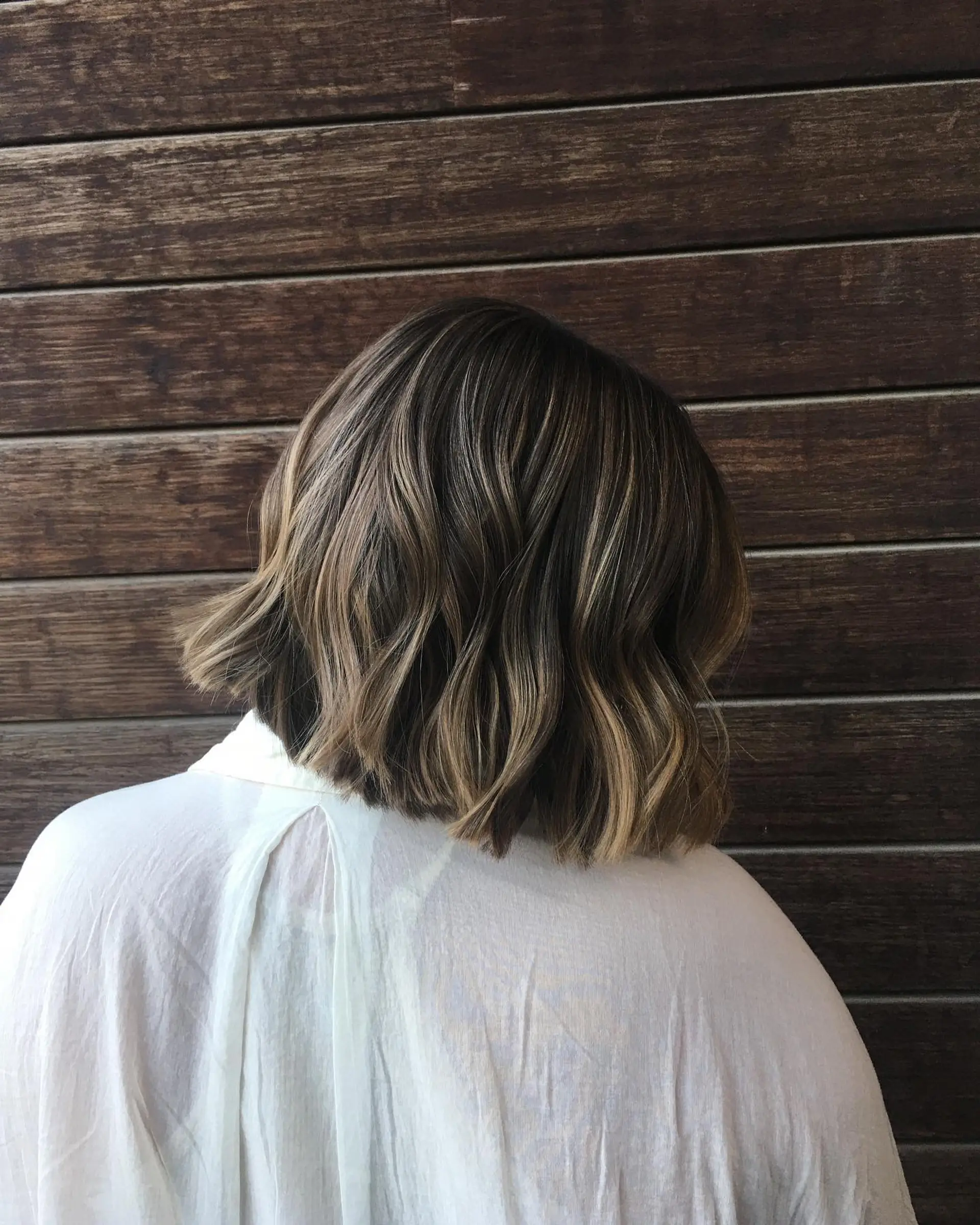 A textured short bob styled in soft waves with fine dimensional balayage highlights. 1
