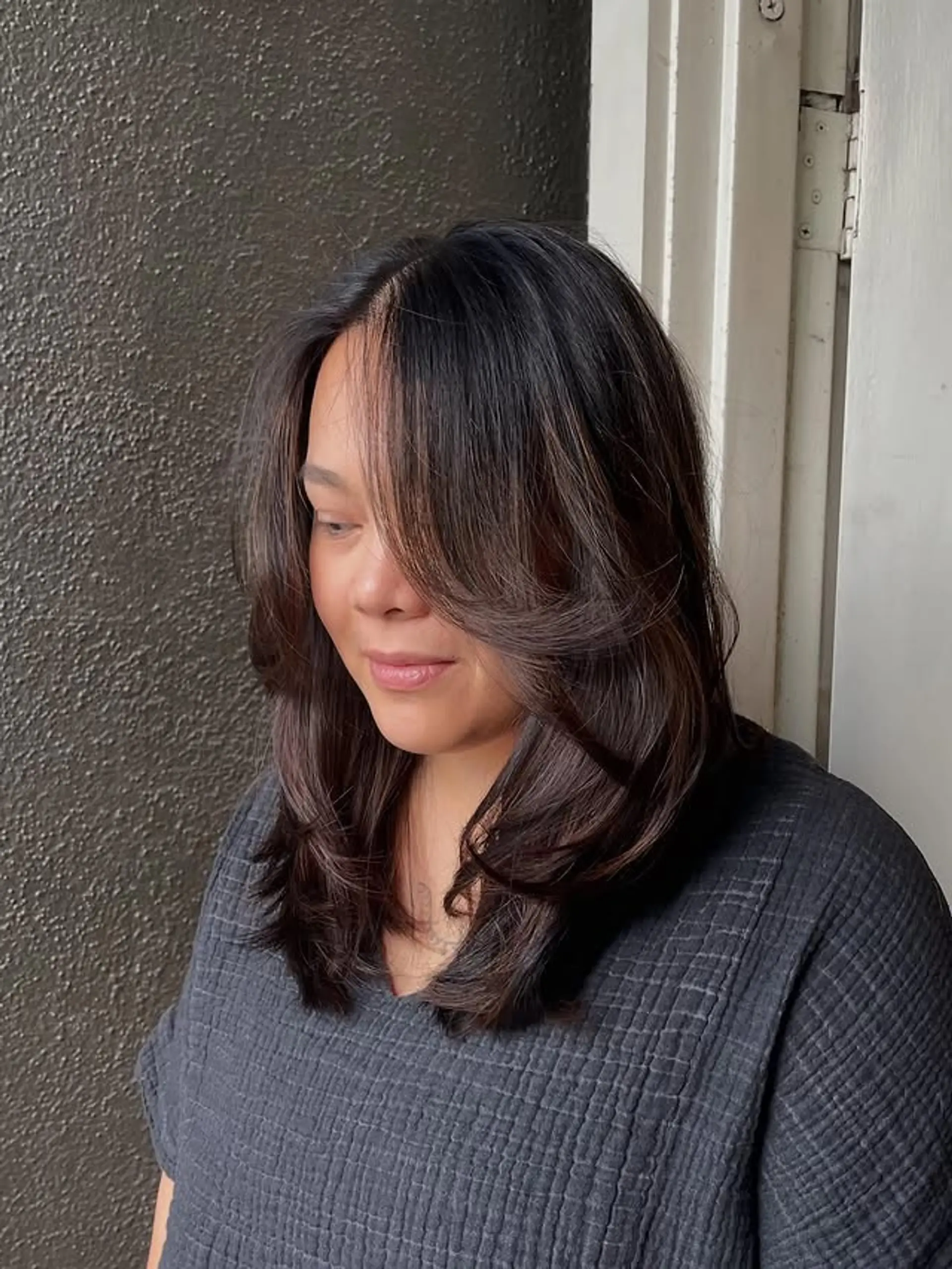 A medium length layered haircut with face-framing pieces and a side part. 1