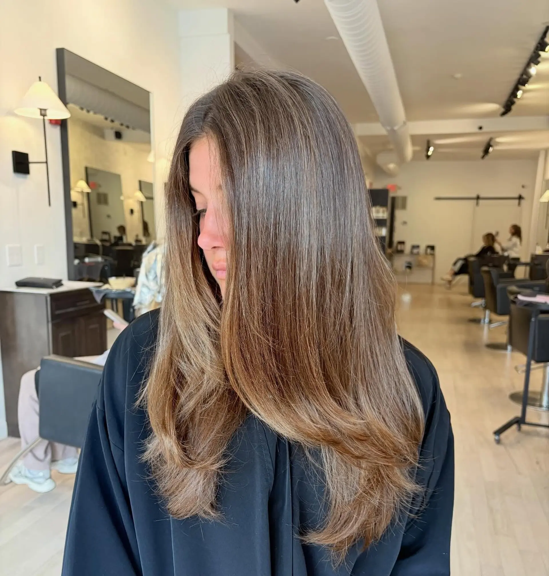 Long dimensional brunette hair styled smooth with softly beveled, face-framing layers. 1