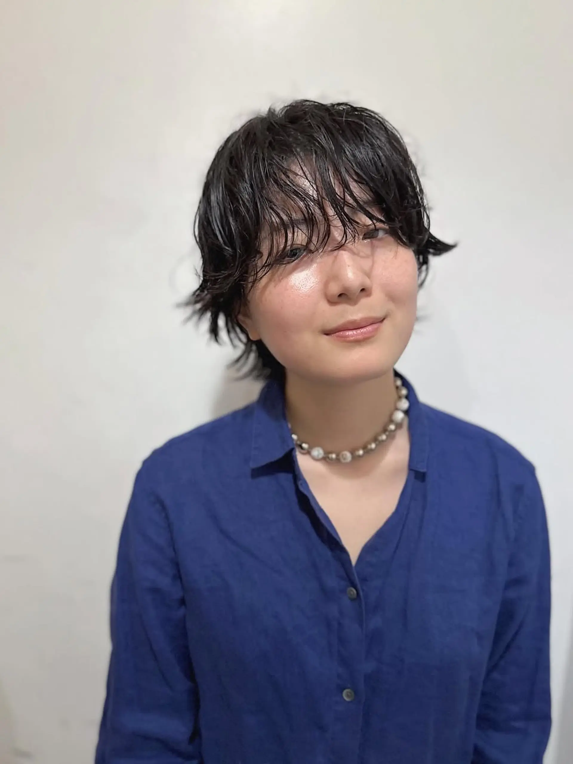 A trendy short textured shaggy pixie cut with soft, wavy bangs. The layers are strategically cut to create movement and volume, giving it a modern, undone aesthetic. This cut is versatile and can be styled with a wet-look or more natural finish. 1