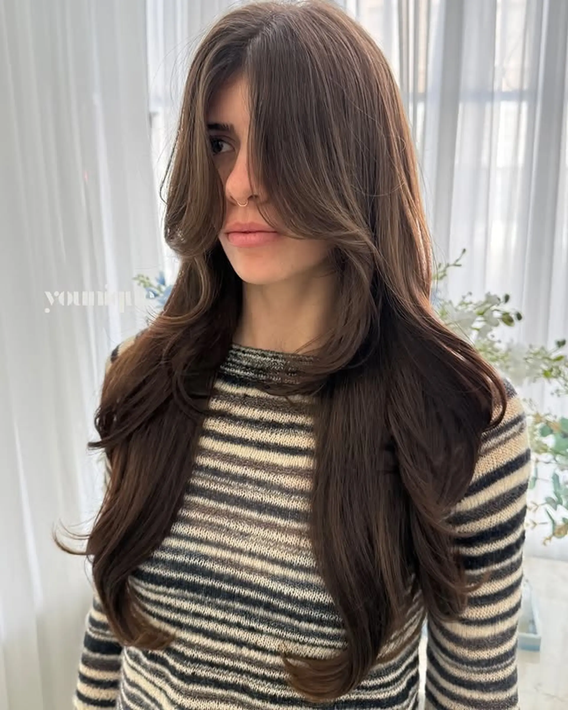 This hairstyle features long layers and face-framing curtain bangs that blend seamlessly into soft waves. 1