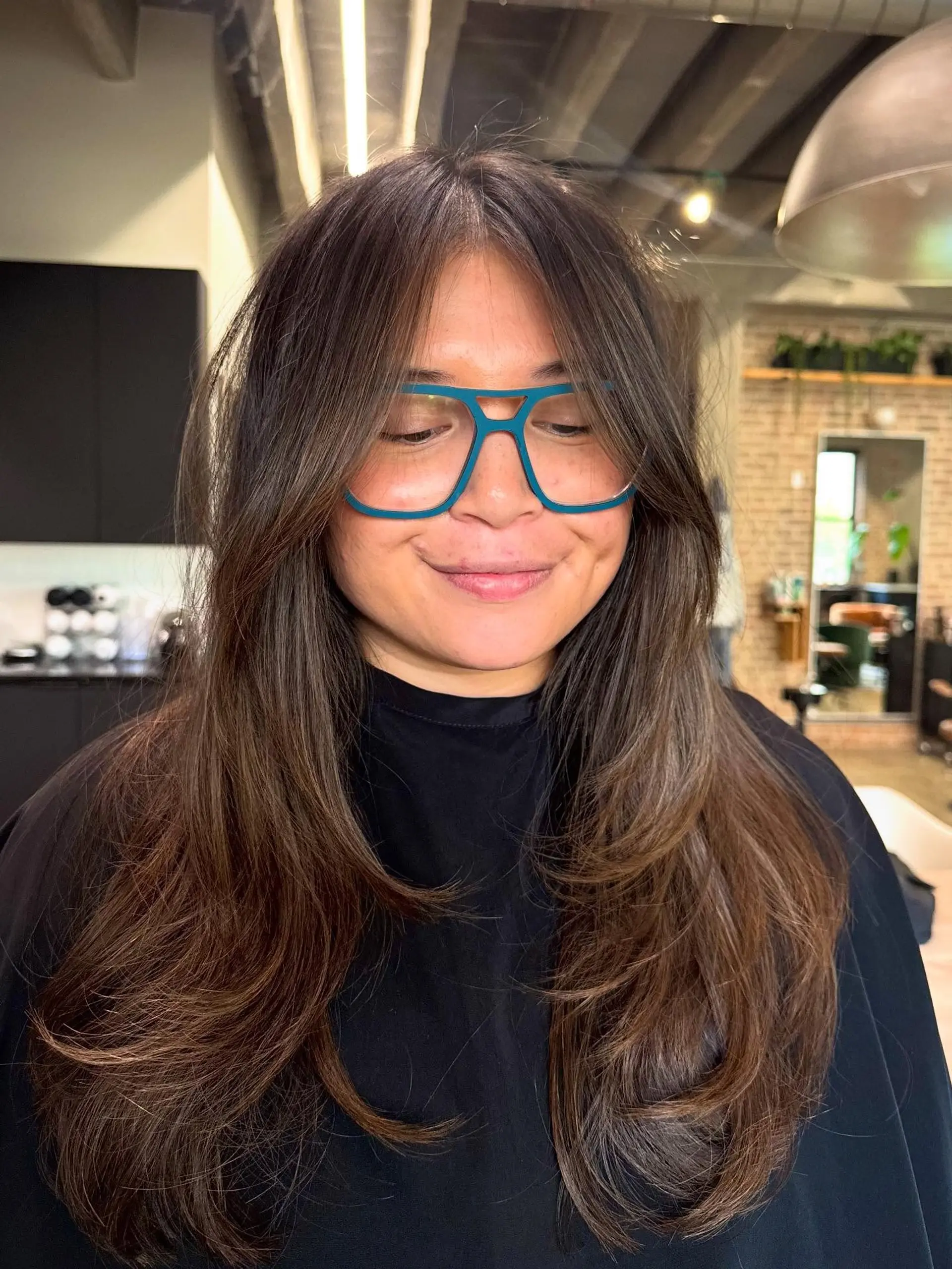 This long layered cut features extensive face-framing layers and curtain bangs, creating soft volume and movement throughout the hair. The ends are texturized and appear bouncy. 1