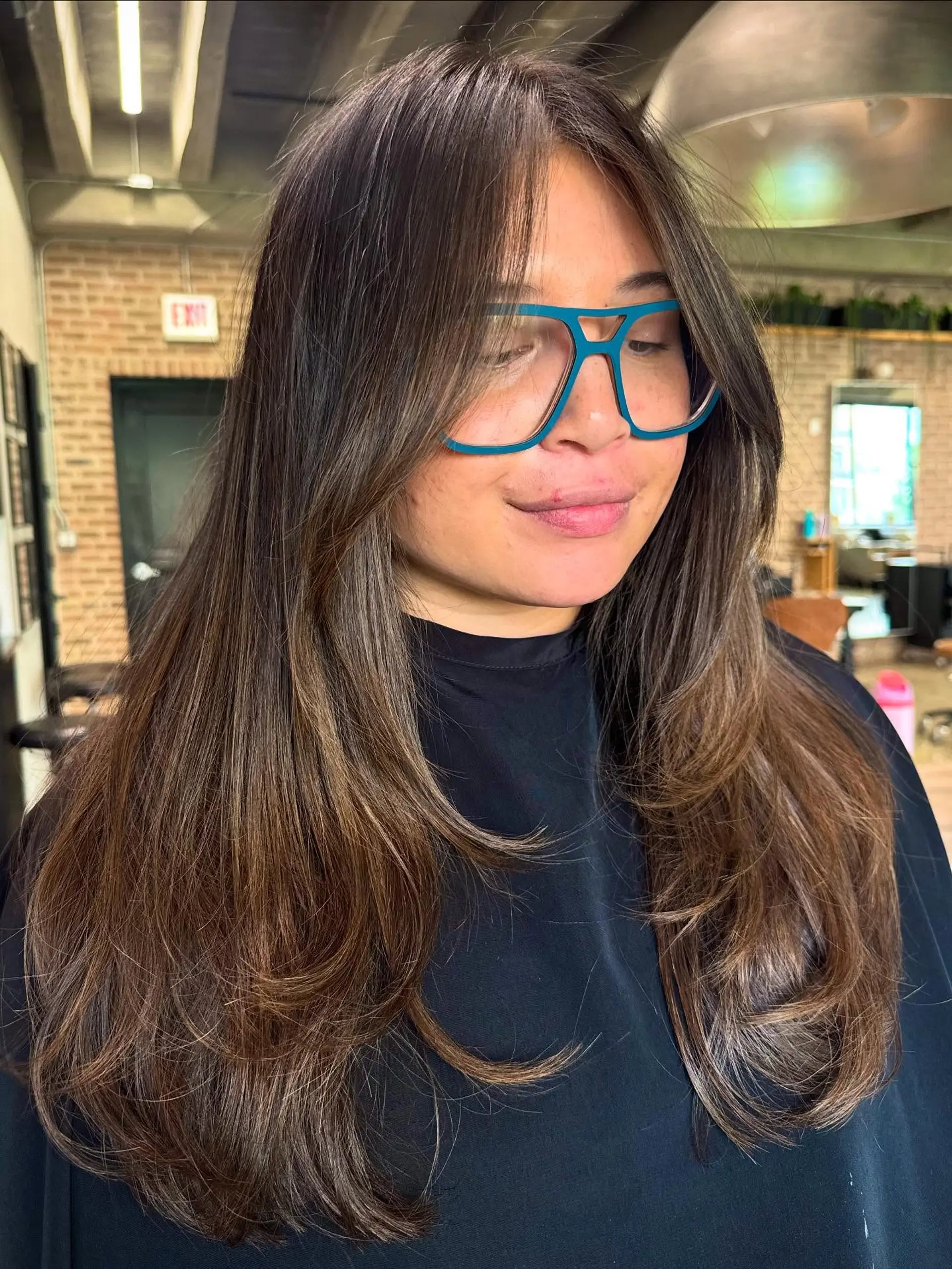 This long layered cut features extensive face-framing layers and curtain bangs, creating soft volume and movement throughout the hair. The ends are texturized and appear bouncy. 4