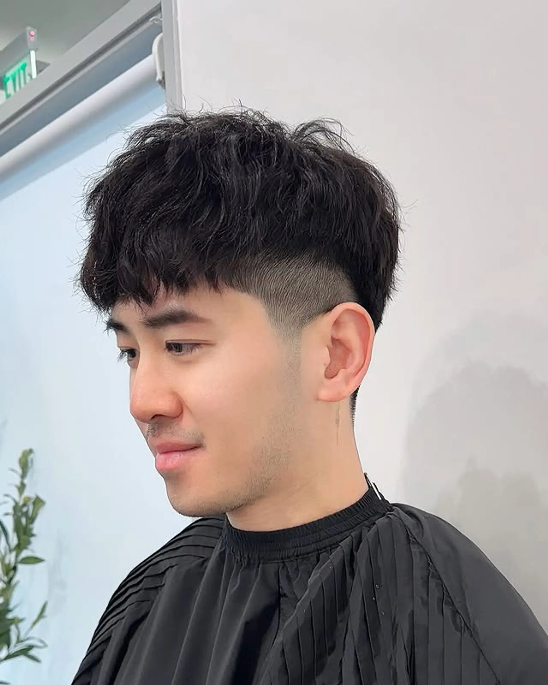 A fresh textured crop top with a sharp undercut fade on the sides and back, featuring naturally wavy hair styled forward into a short, choppy fringe for a modern and edgy aesthetic. 1