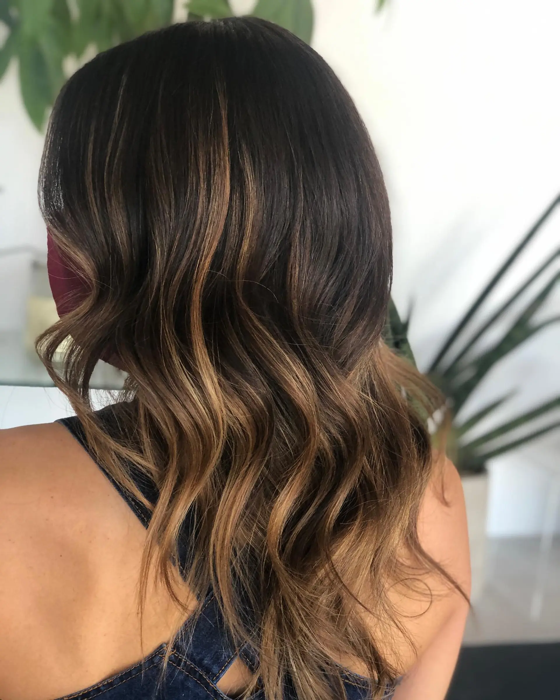 Dark brunette hair featuring dimensional caramel balayage ribbons, styled in soft, cascading waves. 1