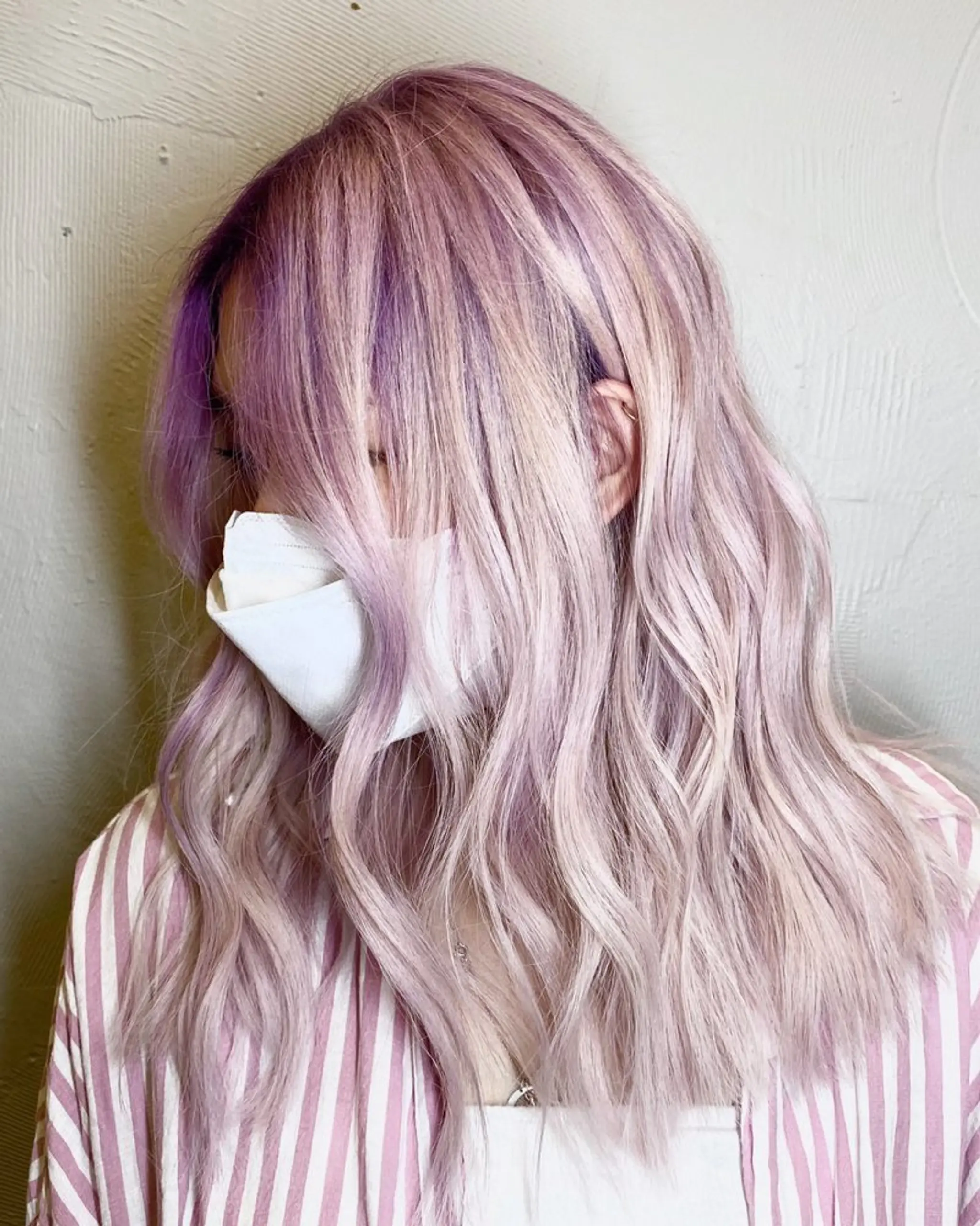 Medium-length wavy hair with a blend of lavender and pastel pink colors, featuring an ombre effect and soft, flowy waves.