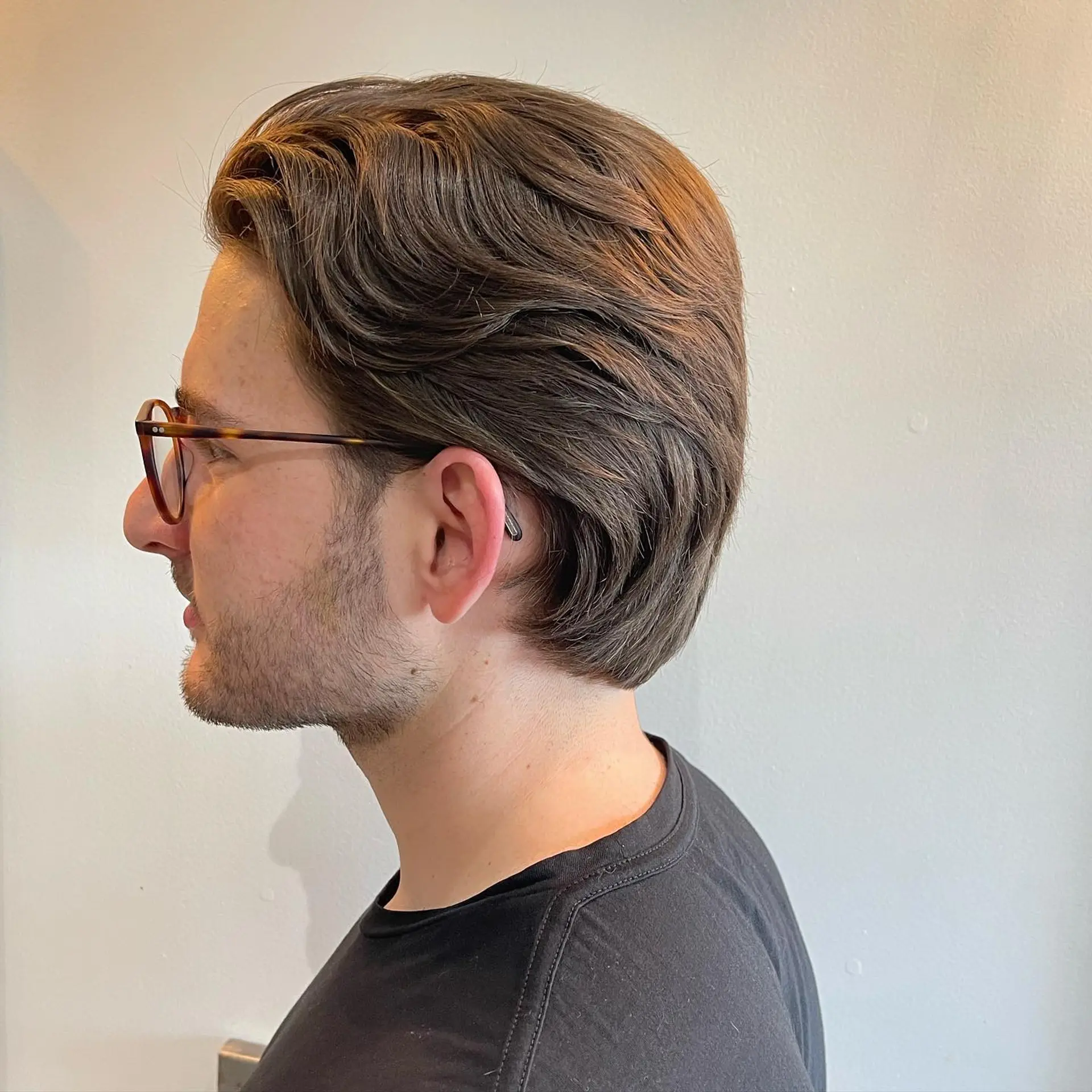 A tailored men's haircut with soft layering and natural flow brushed back around the ears. 1
