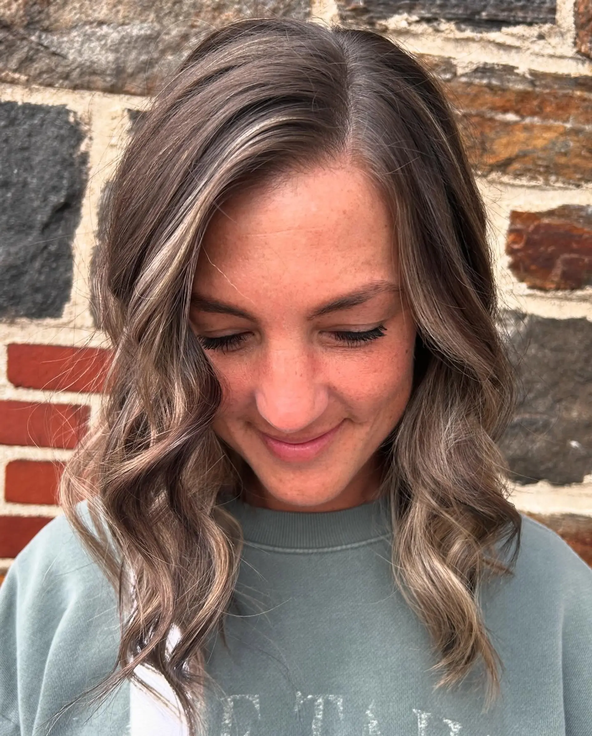 Collarbone-length hair colored with blended lowlights and blonde highlights, styled in loose dimensional waves. 1