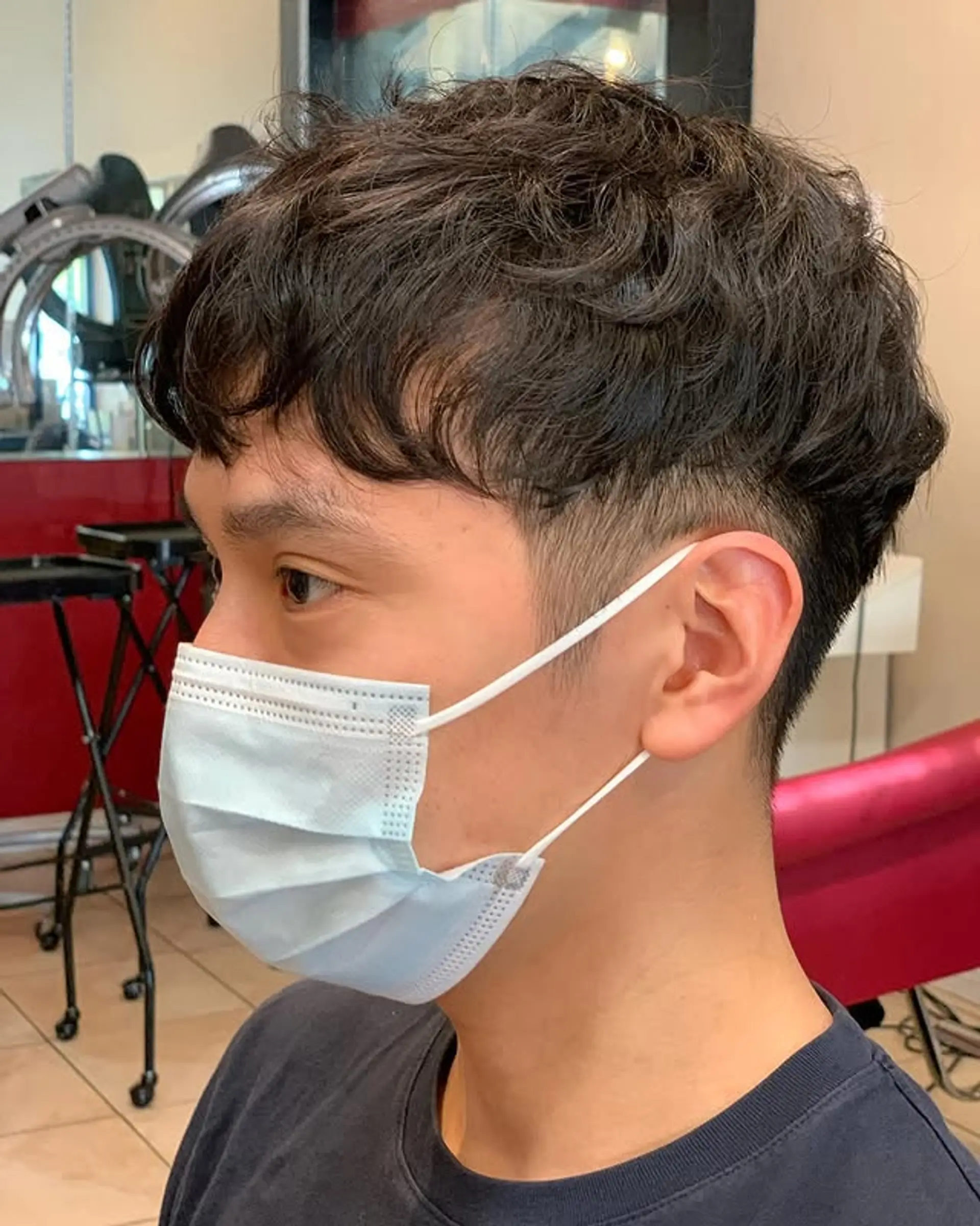 This is a trendy men's short hairstyle with faded sides and back, creating an undercut effect, while the top hair is styled with soft, natural-looking waves and a textured fringe that falls casually on the forehead. 1