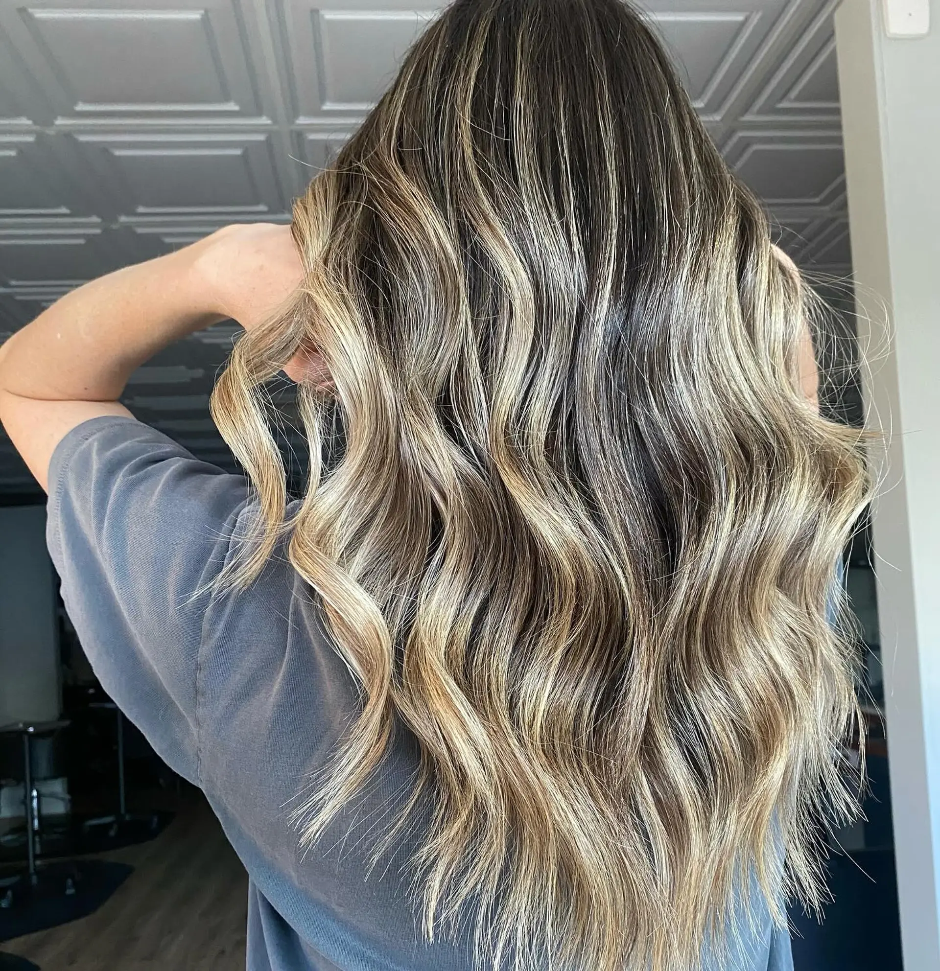 Long wavy hair featuring a dark natural base blended with cool and warm dimensional blonde balayage highlights. 1