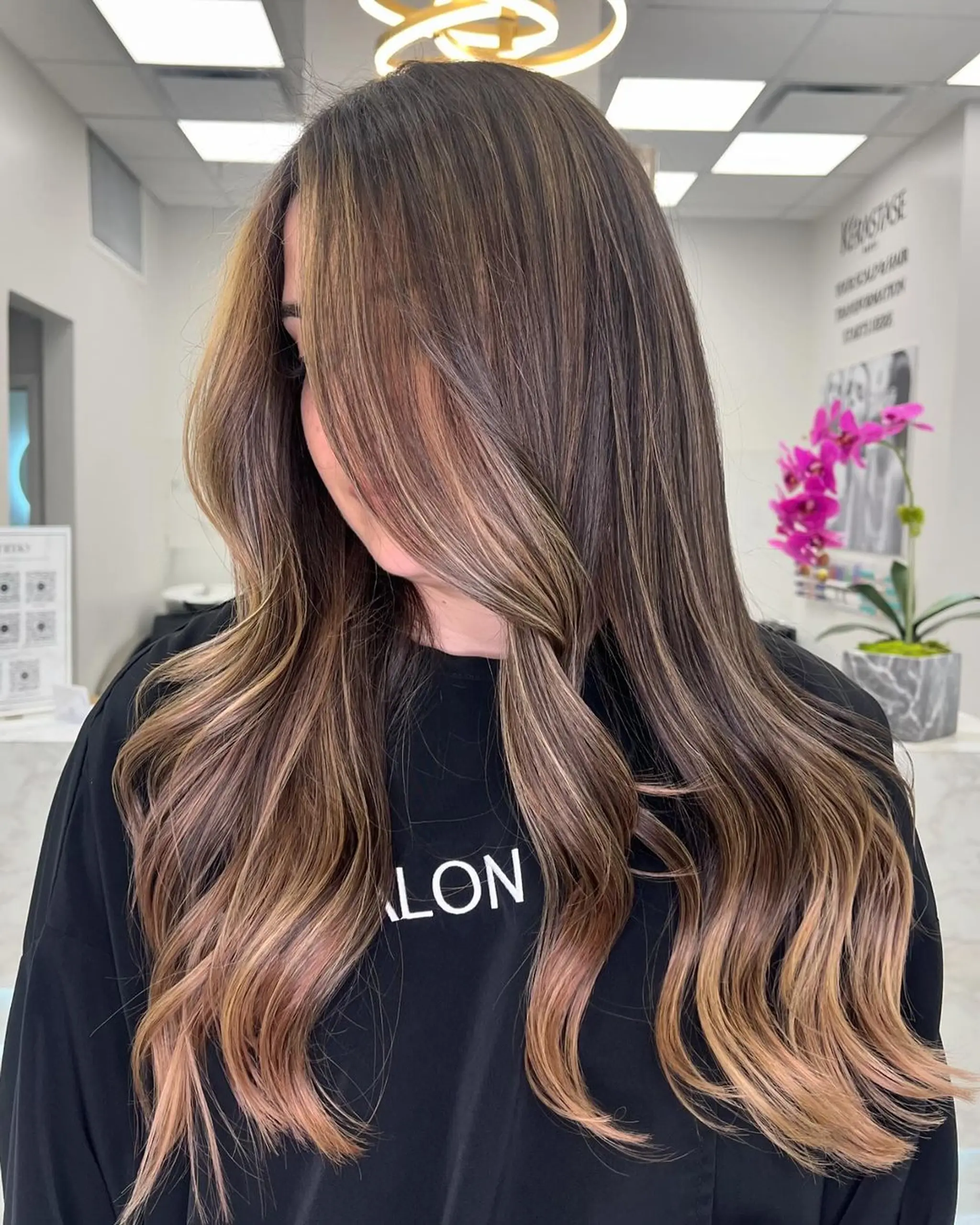 A long, wavy hairstyle with balayage featuring brown, blonde, and caramel colors. Includes layered and face-framing sections for added dimension.