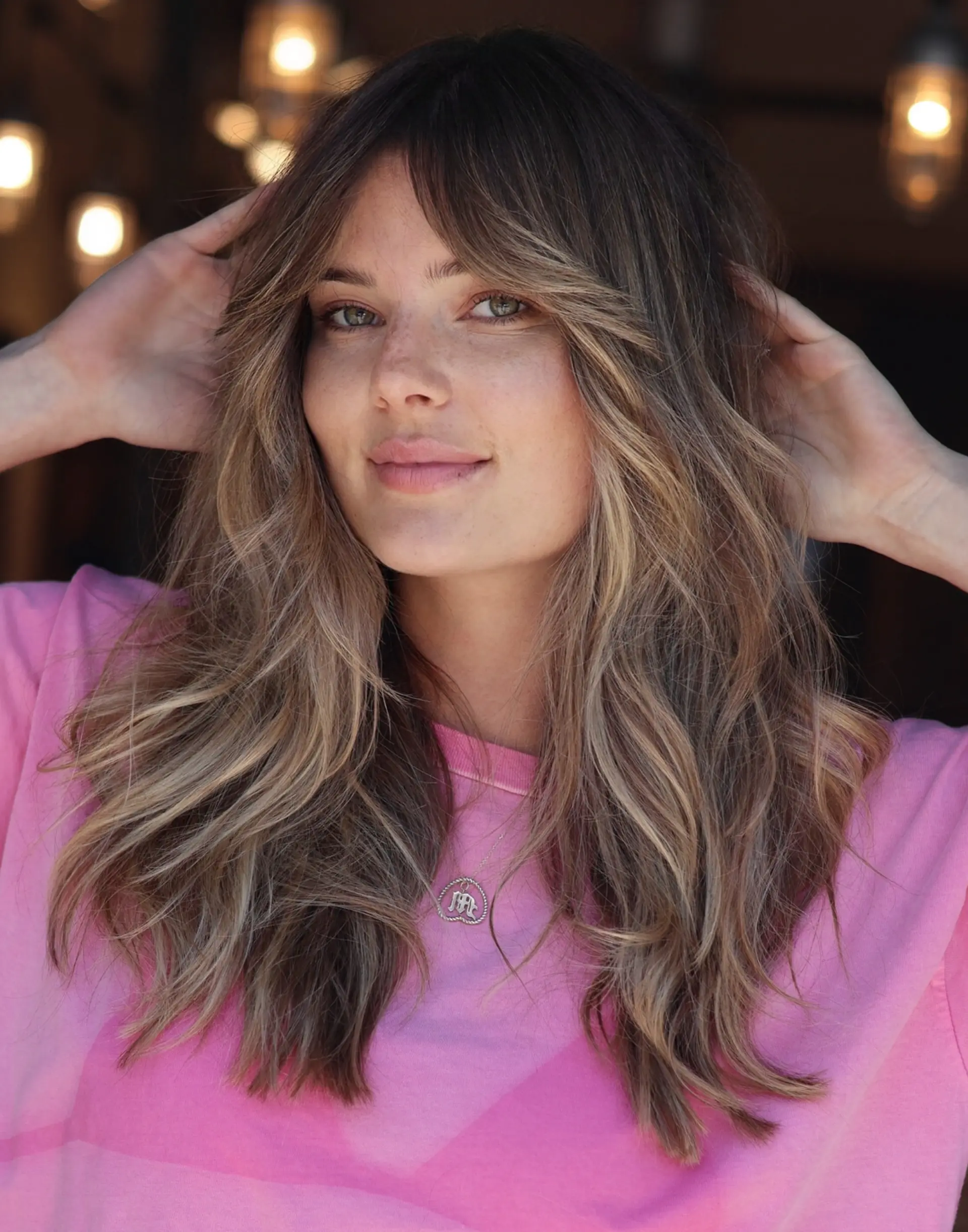 Long layered haircut featuring 70s-inspired curtain bangs and soft waves with dimensional blonde highlights. 1
