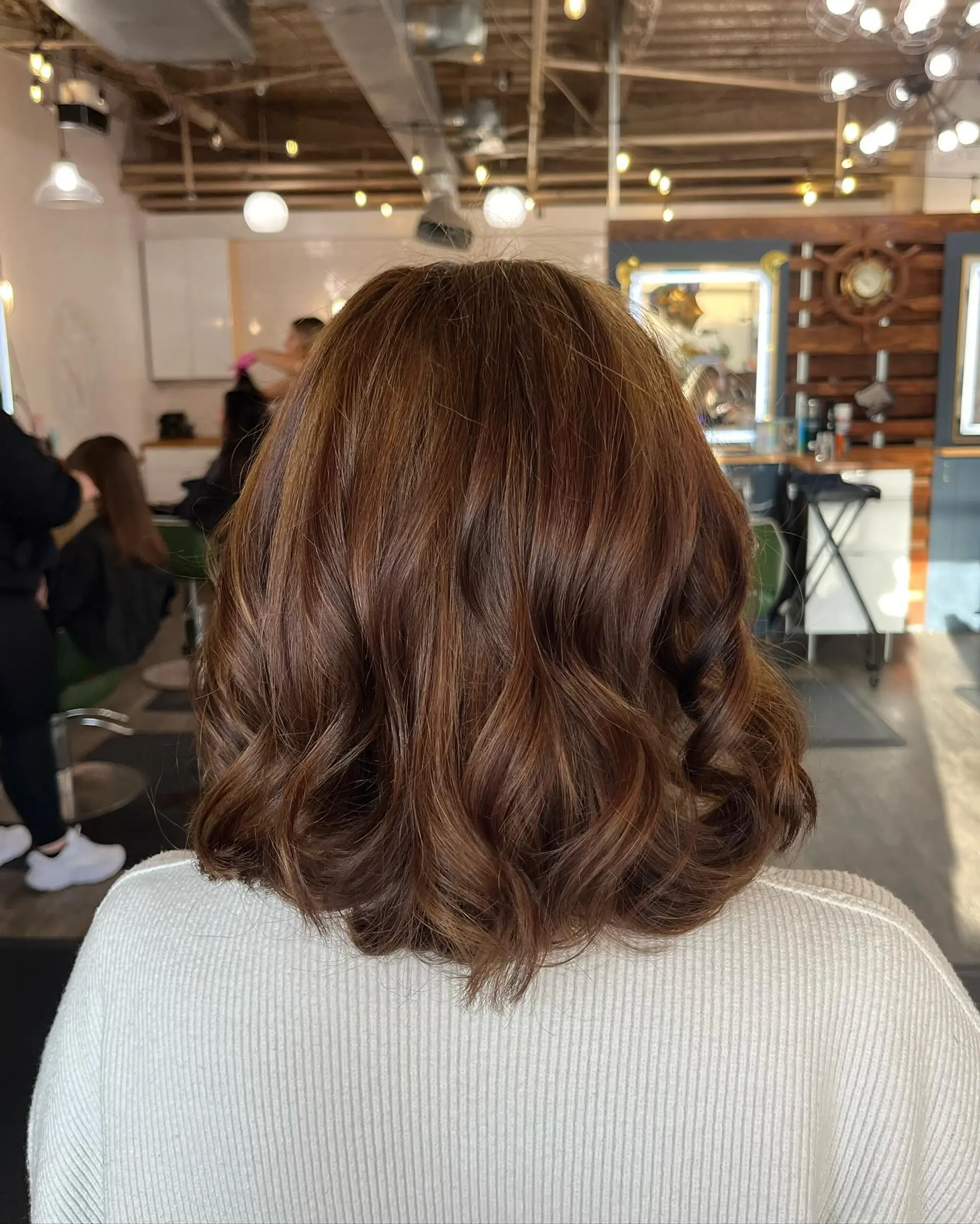 A textured shoulder-length lob styled with loose, bouncy waves in a rich warm brown hue. 1
