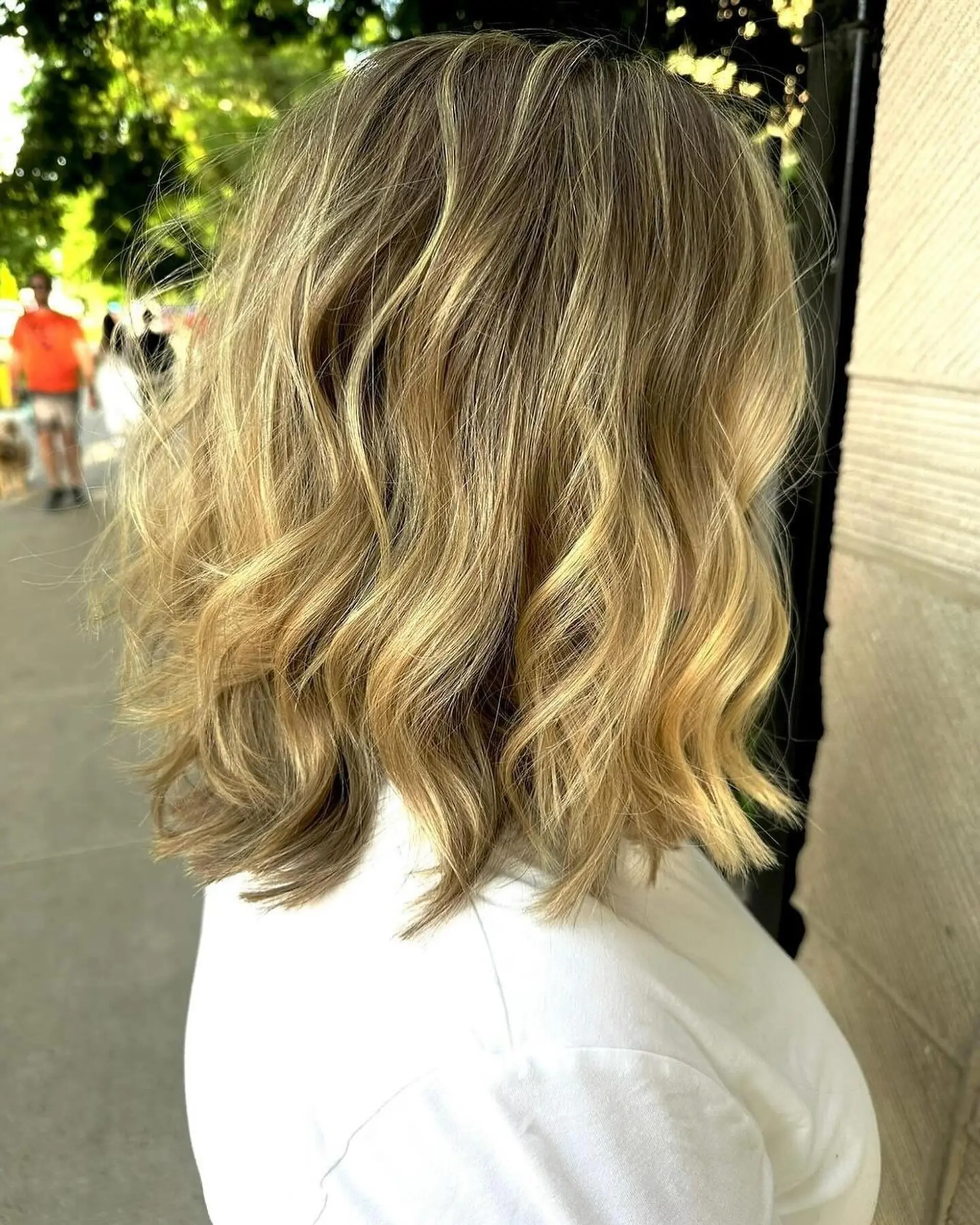 A shoulder-length lob styled in soft, relaxed waves showcasing fine blonde highlights throughout a natural light brown base. 1