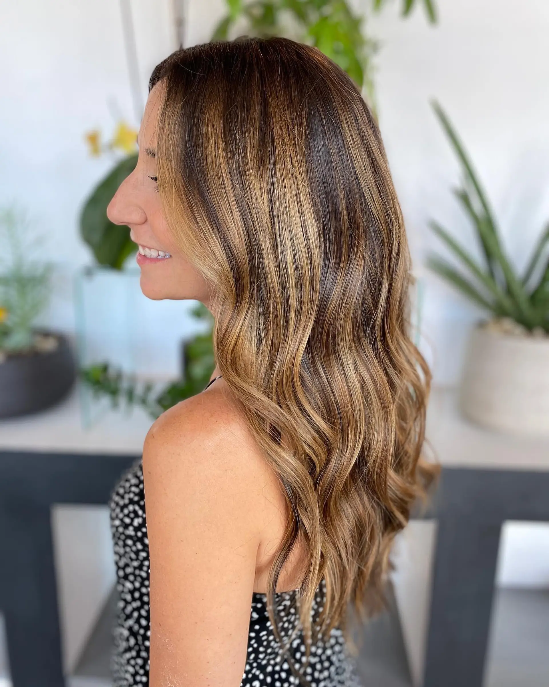 Long wavy brunette hair highlighted with multi-dimensional caramel and warm blonde balayage ribbons. 1