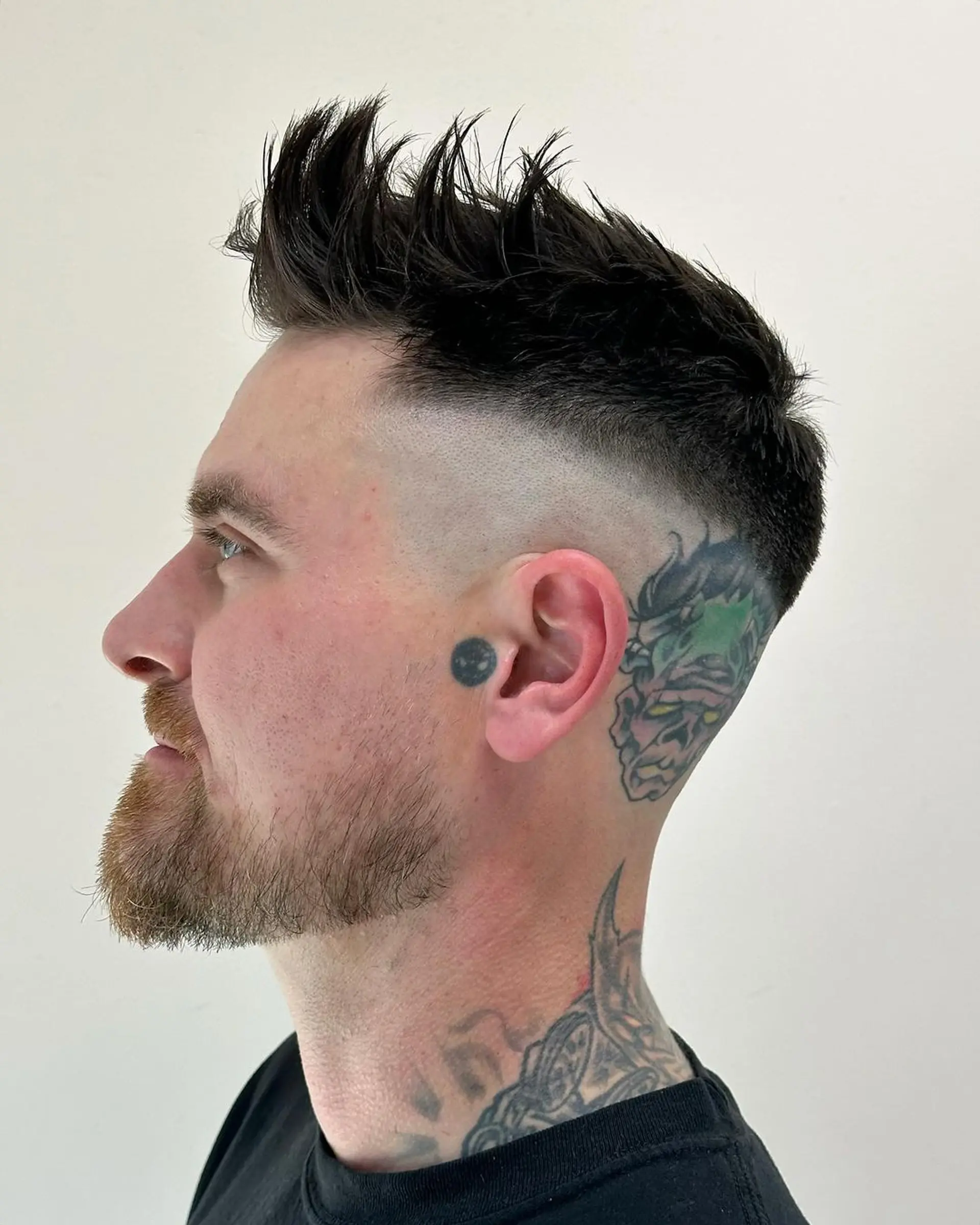 Textured, straight black hair styled into bold spikes with a high fade, offering a punk aesthetic. Short length enhances edge with neat beard alignment. 1