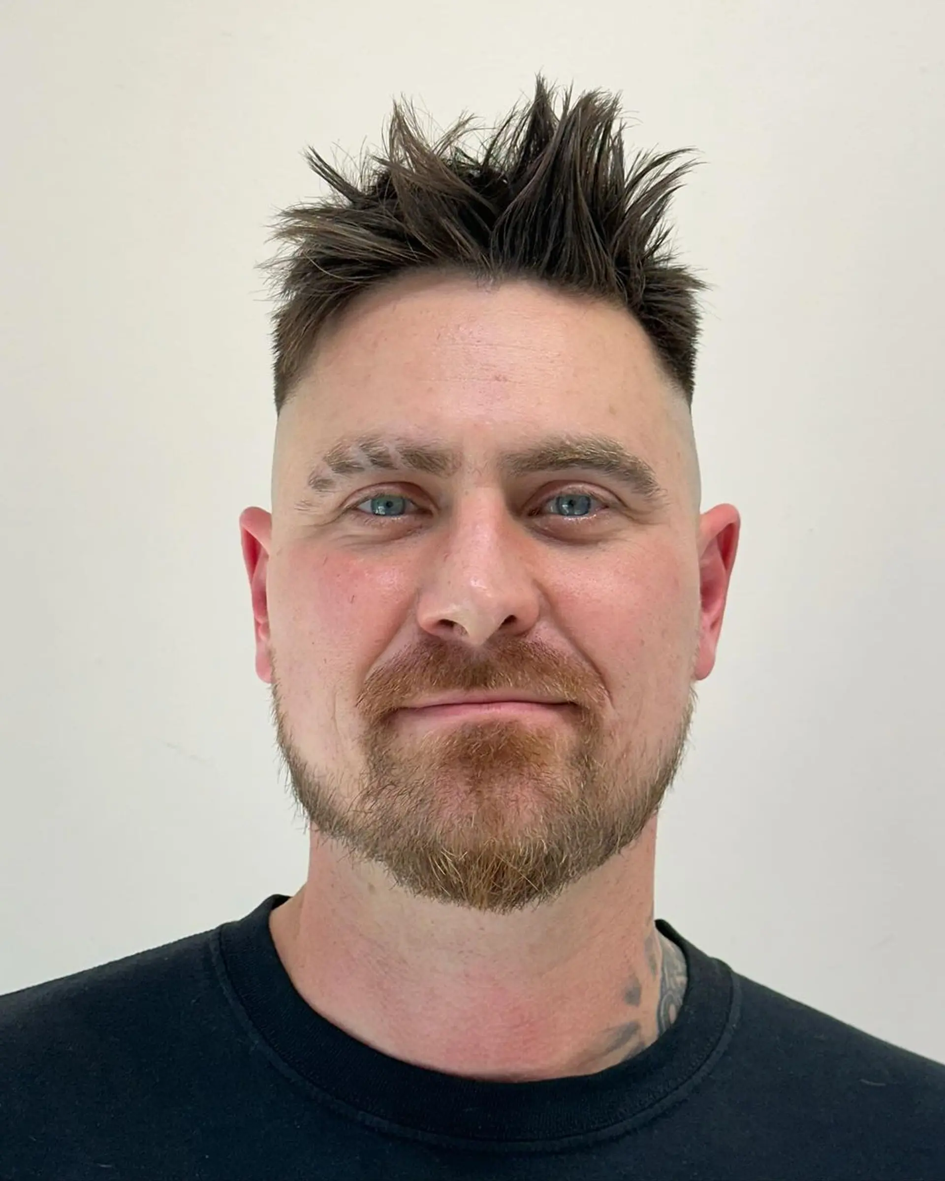 Textured, straight black hair styled into bold spikes with a high fade, offering a punk aesthetic. Short length enhances edge with neat beard alignment. 3