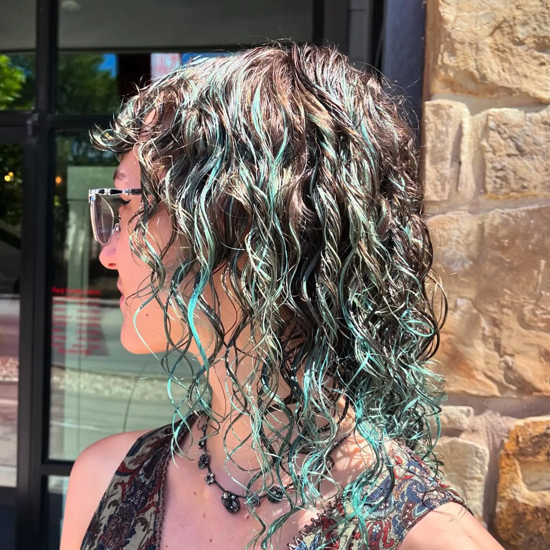 Medium-length layered curly shag cut featuring defined ringlets, textured fringe bangs, and vibrant teal highlights woven throughout dark brown curls. 1