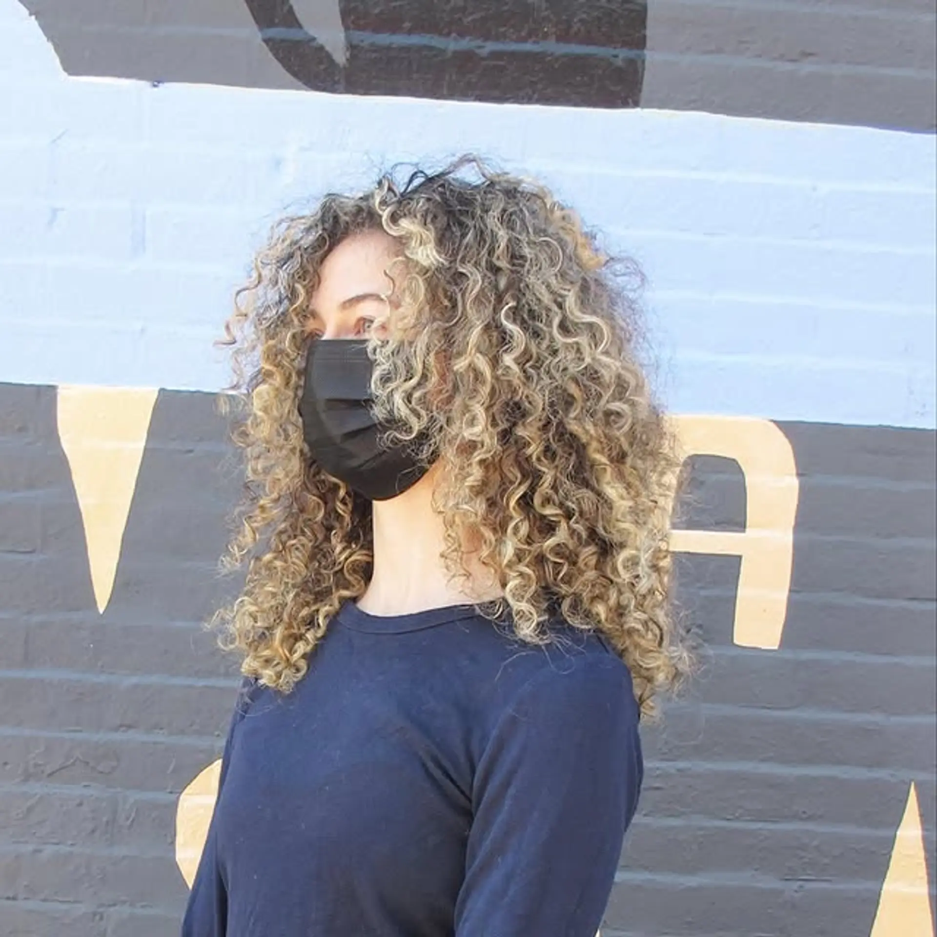 A medium-length curly hairstyle with blonde balayage highlights. 1