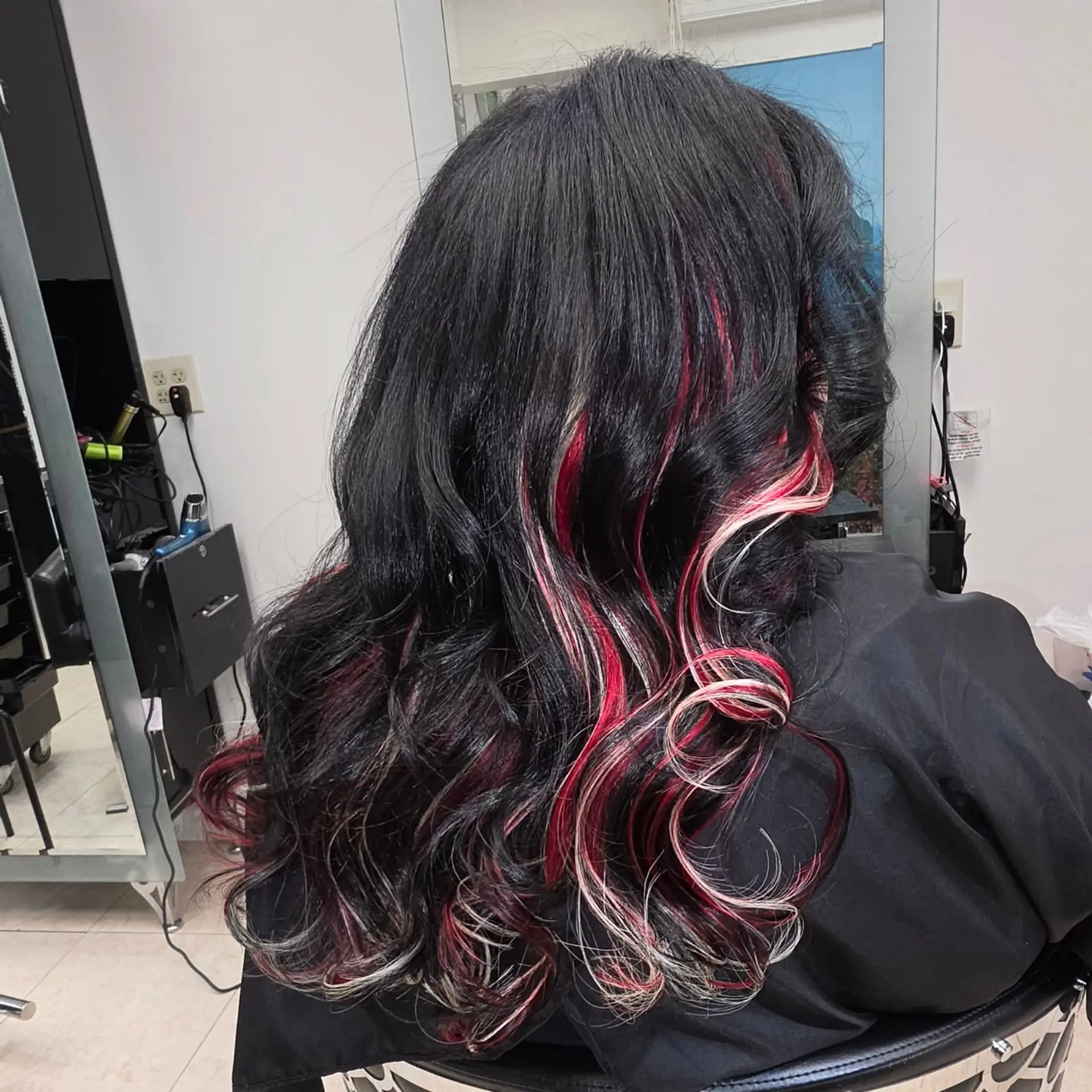 Long wavy black hair styled with vivid red and white peekaboo extension accents woven throughout loose curls. 1