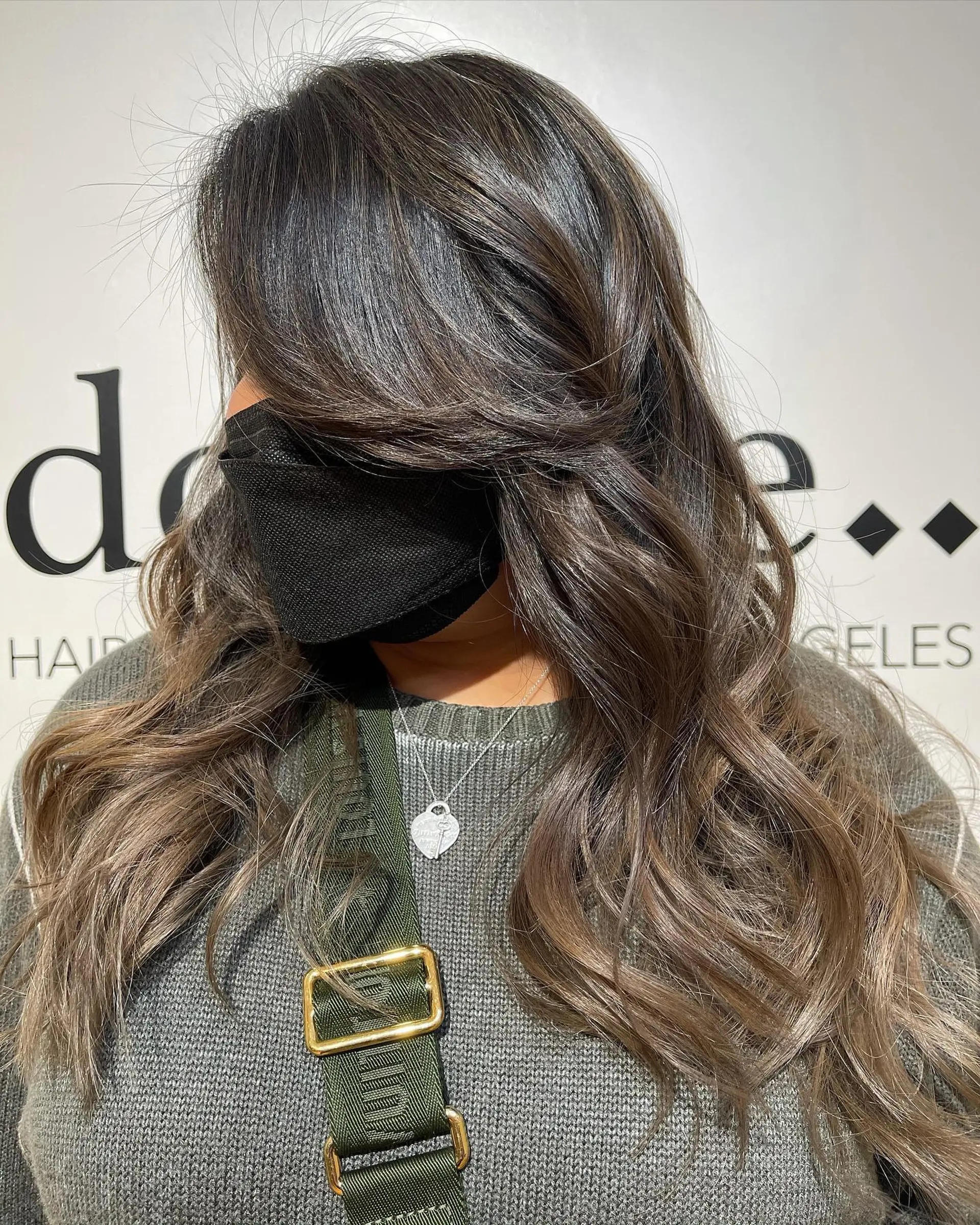 Long layered dark brunette hair with soft ash brown highlights, styled in loose voluminous waves with sweeping curtain bangs. 1