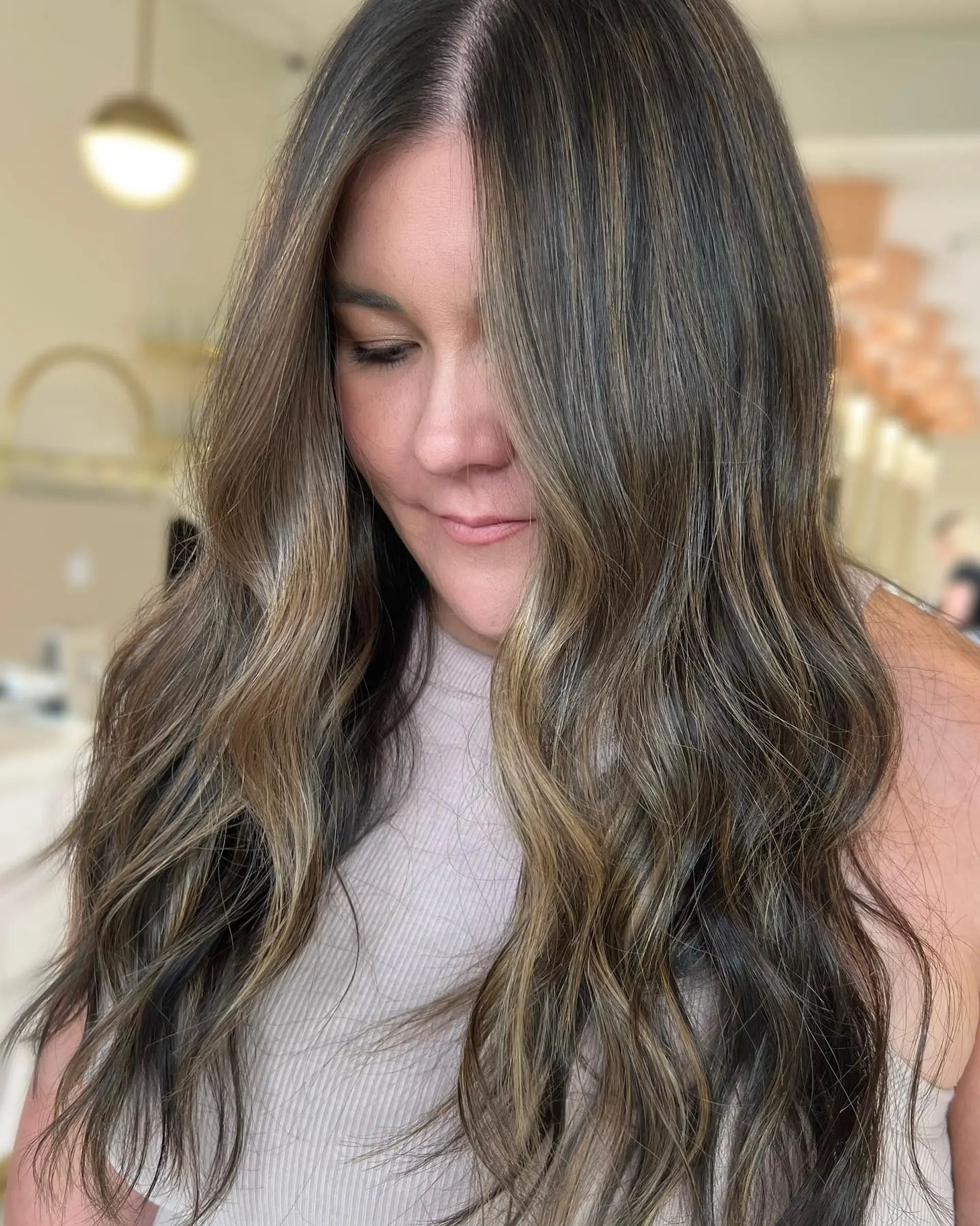 Long dark brunette hair featuring seamless caramel balayage highlights and styled in soft, loose waves. 1