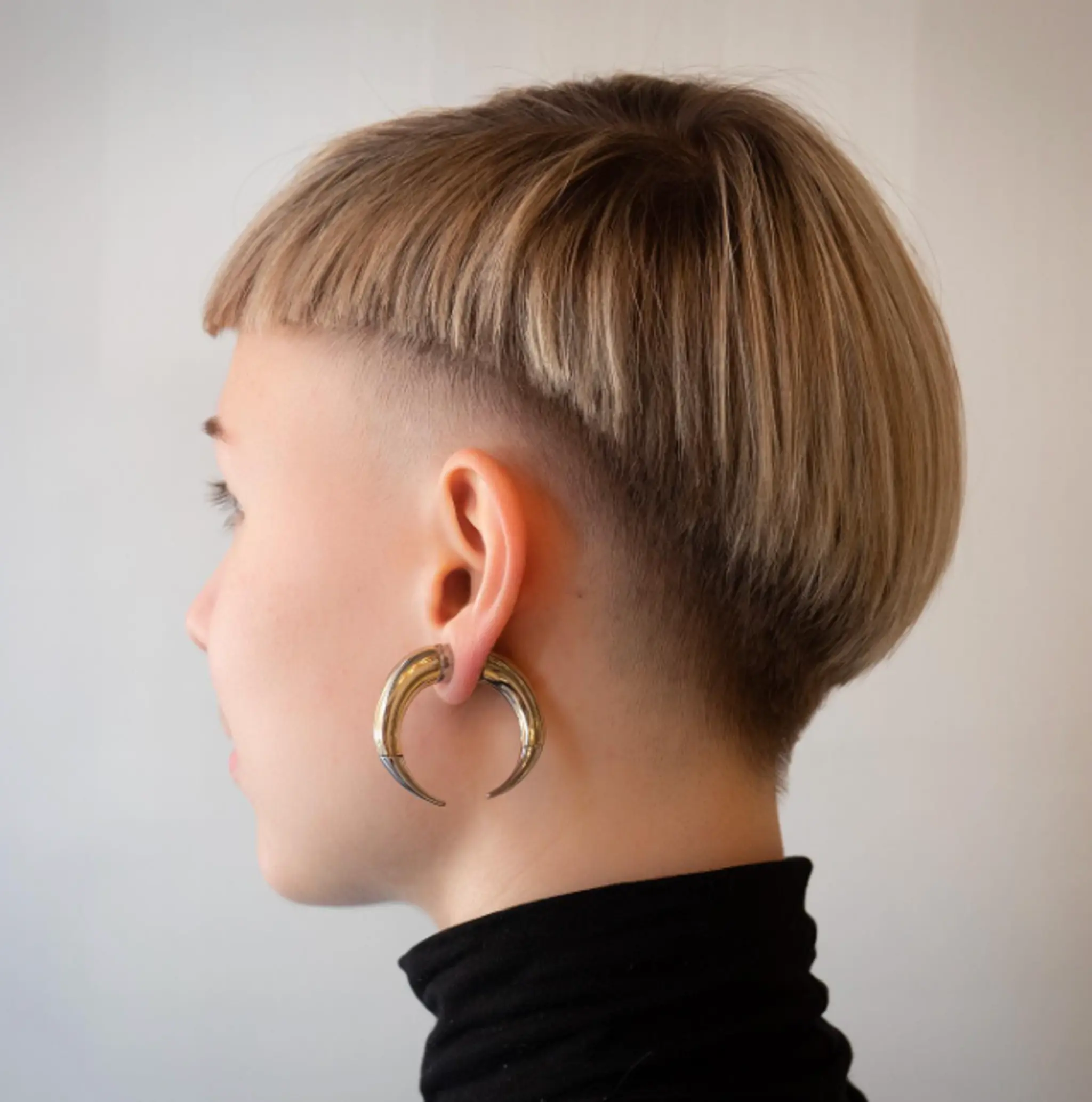 Short and straight hair with a bold undercut and a round, bowl-style cut on top. The fringe is blunt and falls just above the eyebrows, with the overall look being both sophisticated and edgy.