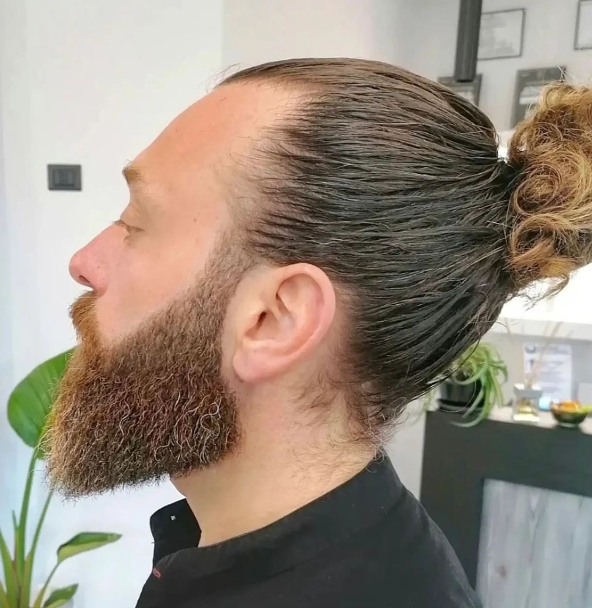 A sleek, polished man bun with wavy brown hair, featuring a tight knot and slicked-back sides. 1
