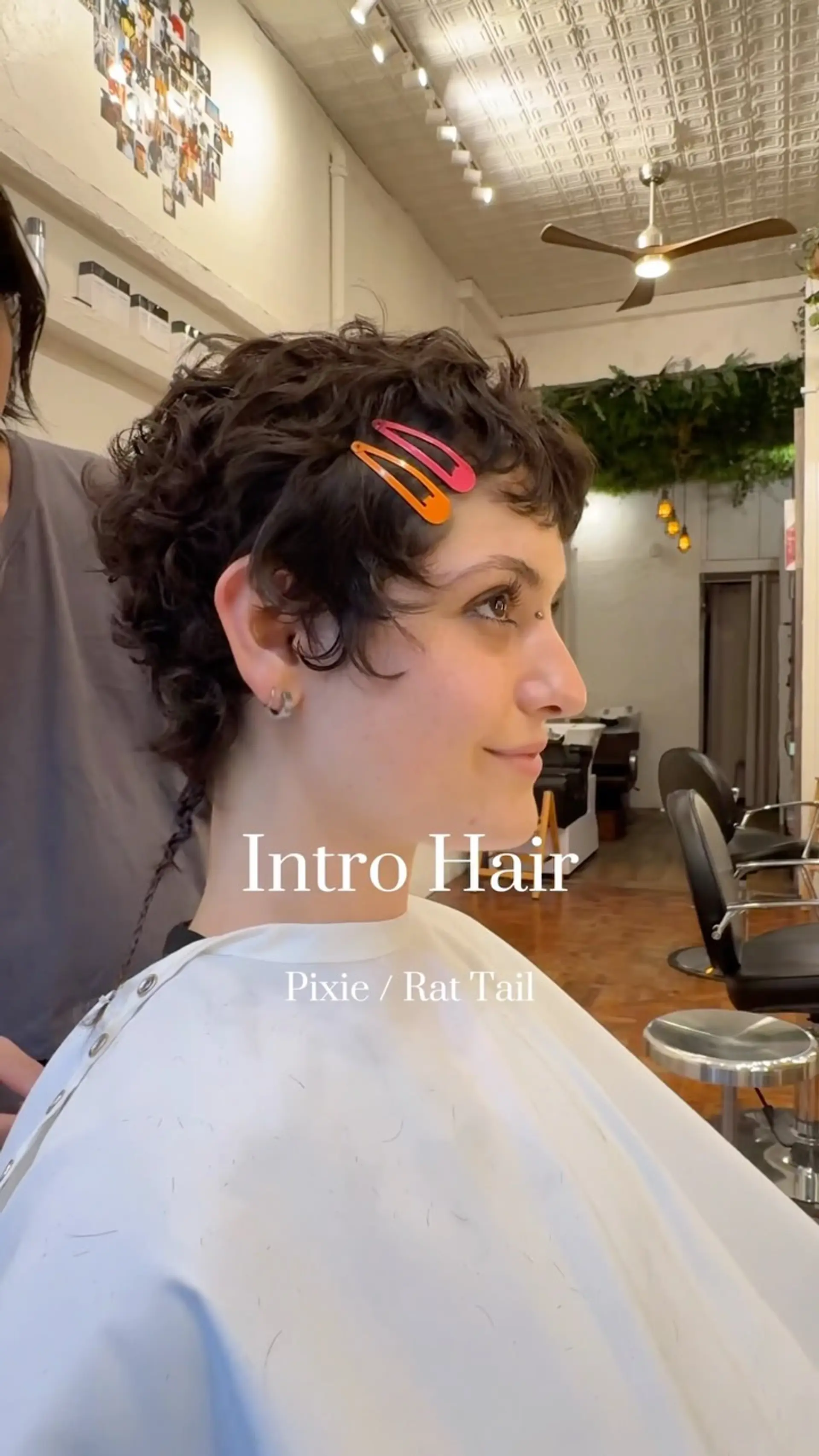 A textured curly pixie haircut styled with soft curls, cropped perimeter, and a delicate braided rat tail at the nape. 1