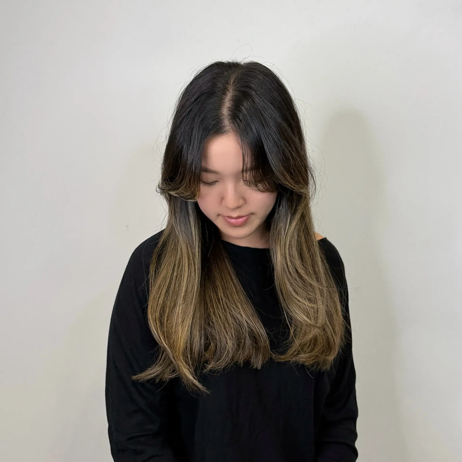 Long layered cut featuring soft curtain bangs and curled ends, highlighted with subtle blonde balayage over a dark brunette base. 1