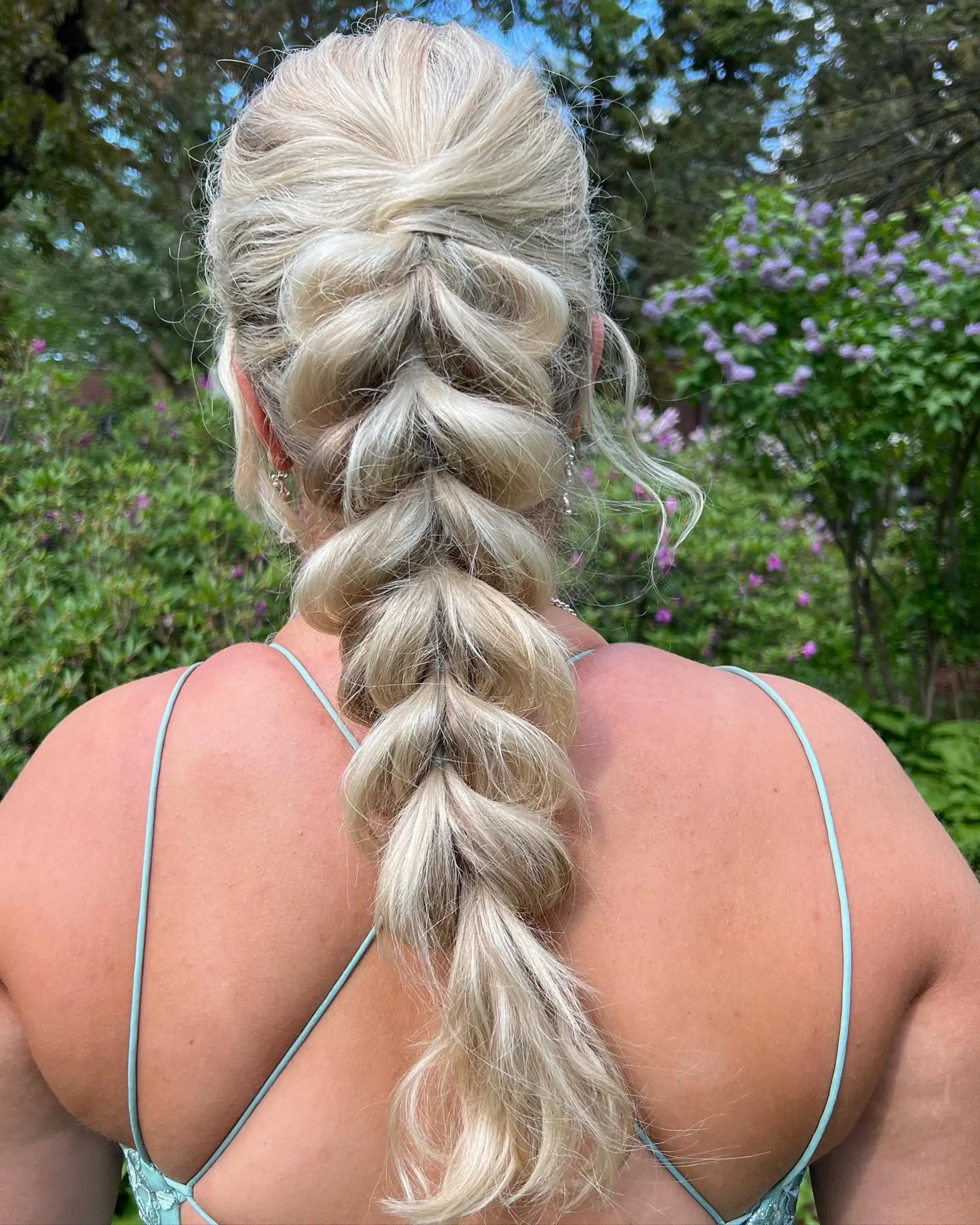 A thick, voluminous blonde pull-through braid styled down the back with soft, textured sections for a formal event. 1