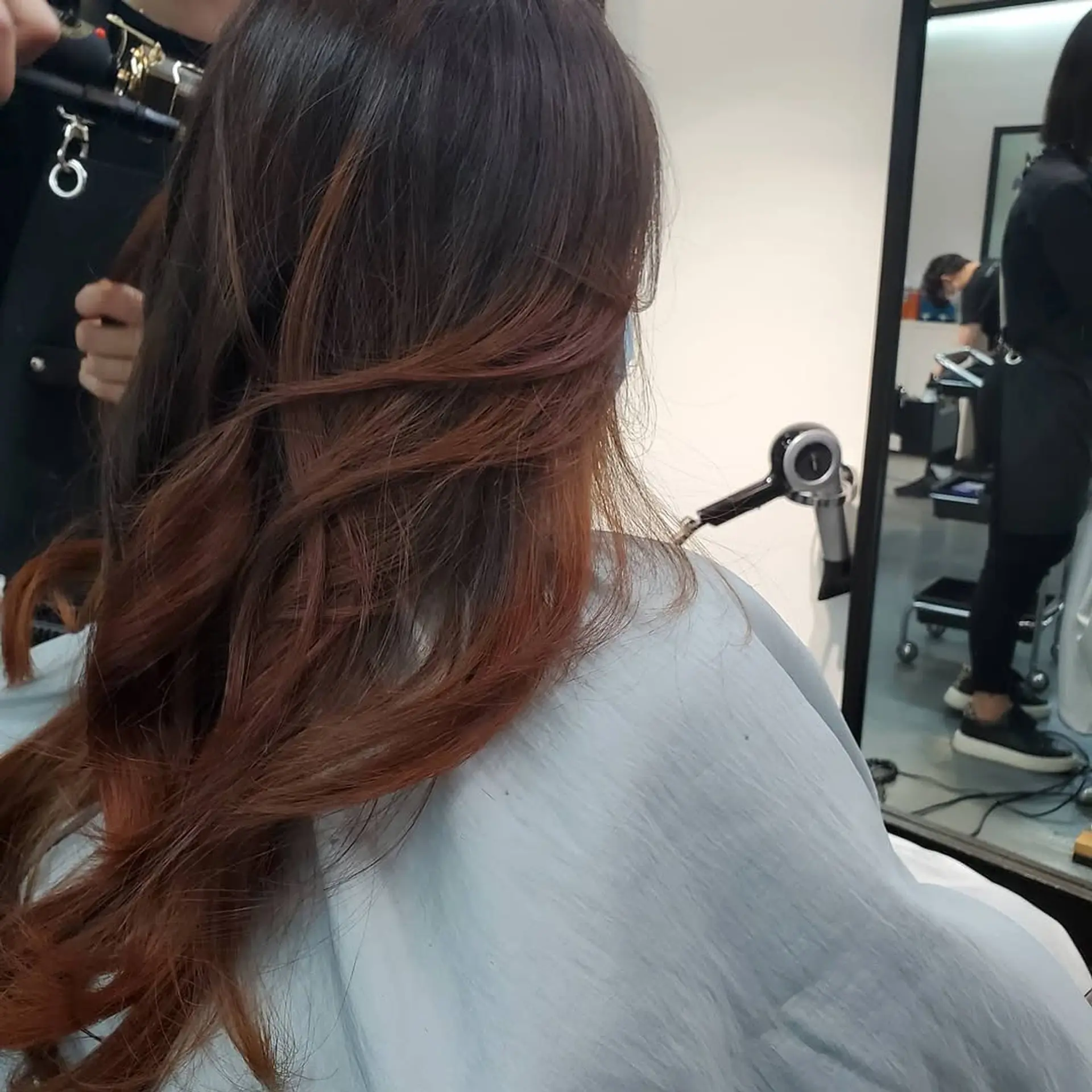 A long, wavy, layered cut featuring a dark base with blended copper and auburn balayage highlights for added depth and dimension. 1