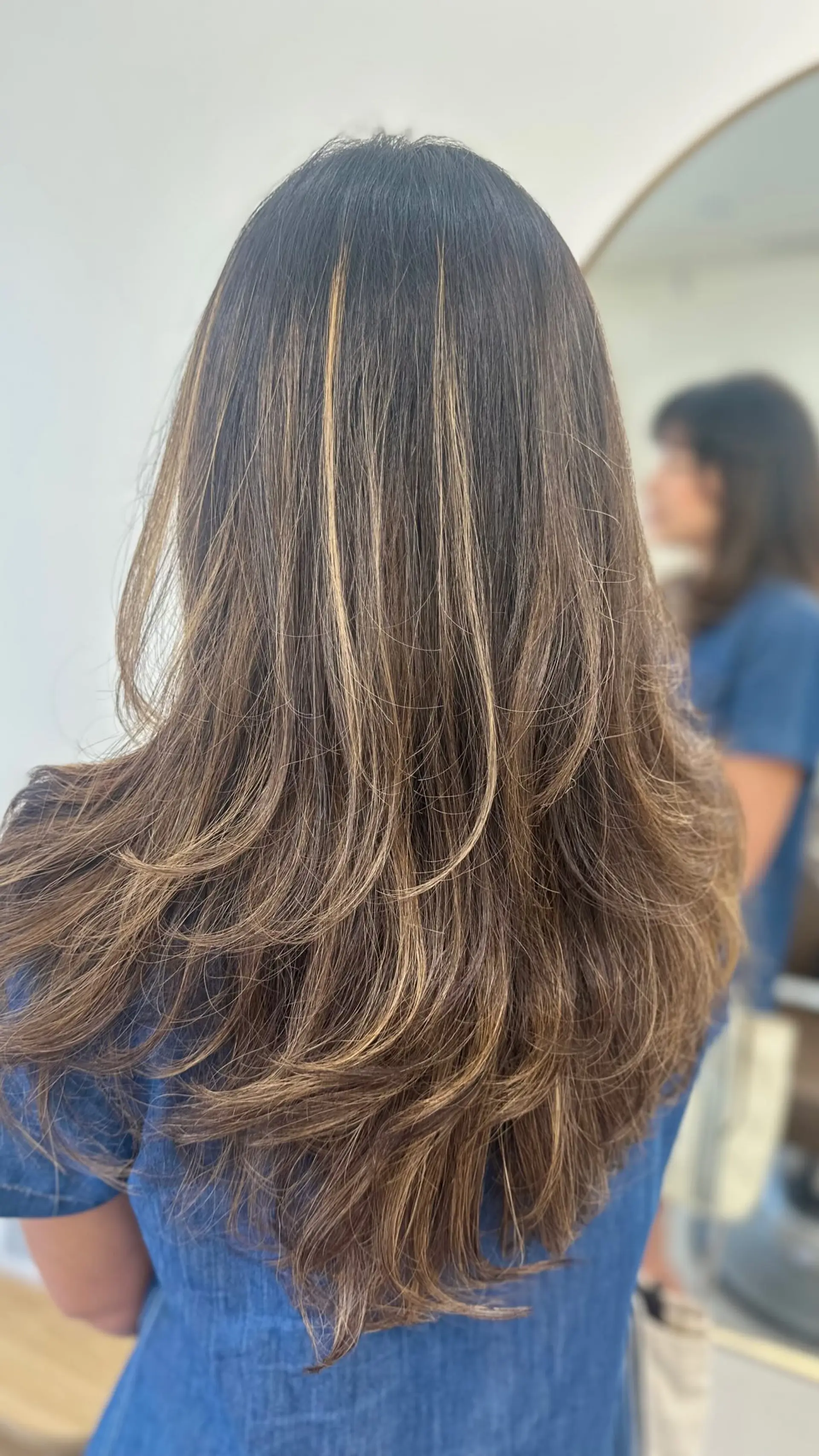 Long brunette hair styled into soft, cascading layers with gentle outward flips and dimensional caramel highlights. 1