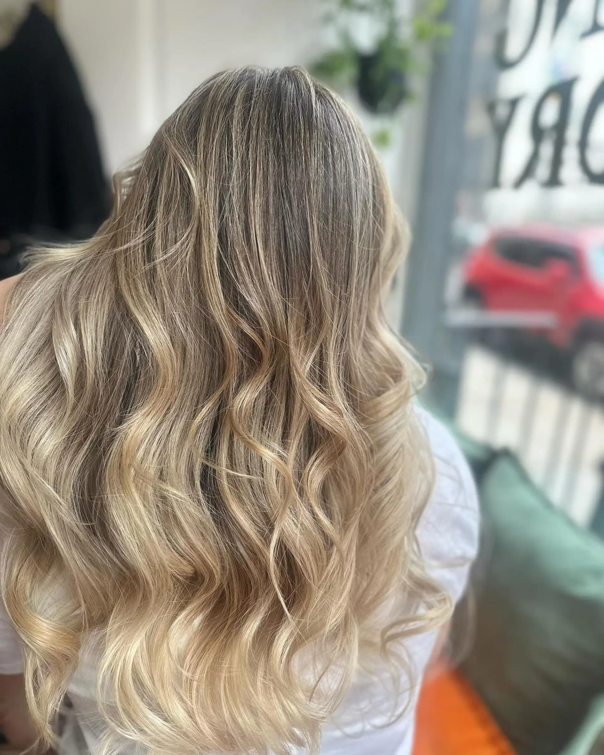 Long, wavy hairstyle with a balayage effect, transitioning from dark blonde and light brown to lighter blonde highlights, featuring loose and natural waves. 1