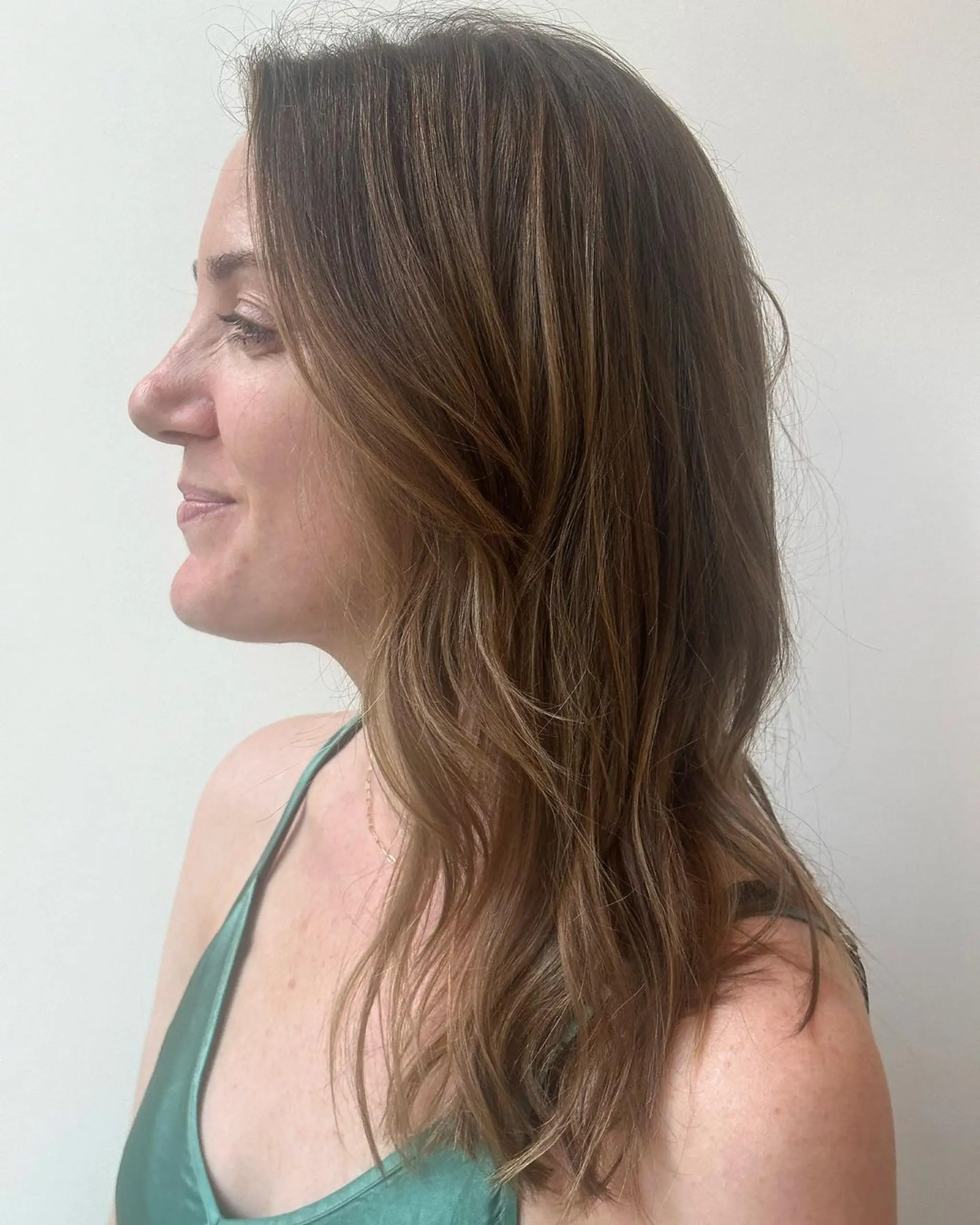 Medium-length wavy hair with light brown color and honey highlights, featuring soft layers that frame the face.