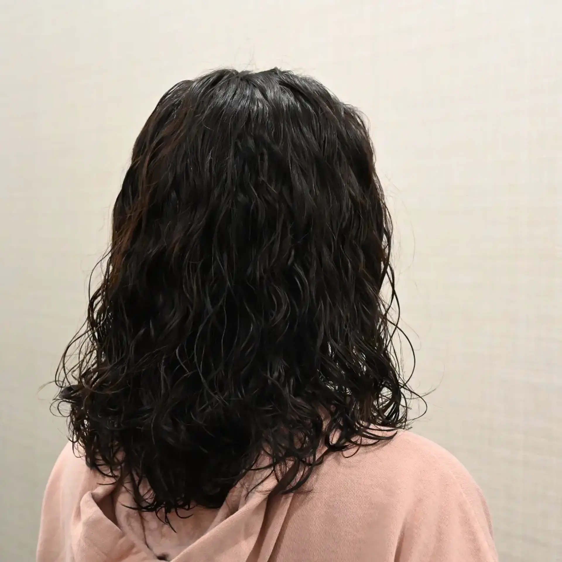 Medium-length dark hair styled with defined wet-look permed waves and curls falling just past the shoulders. 1
