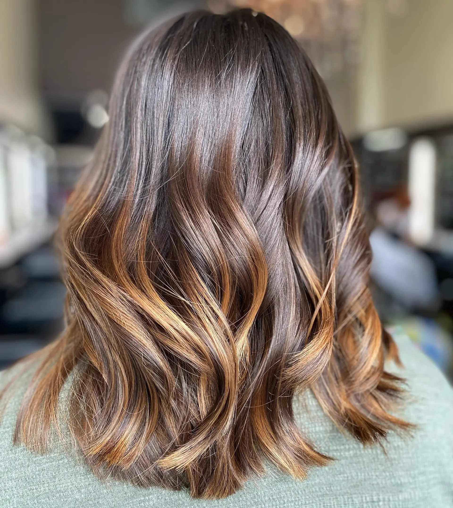 Medium-length brunette lob styled in glossy, soft waves with warm caramel highlights. 1