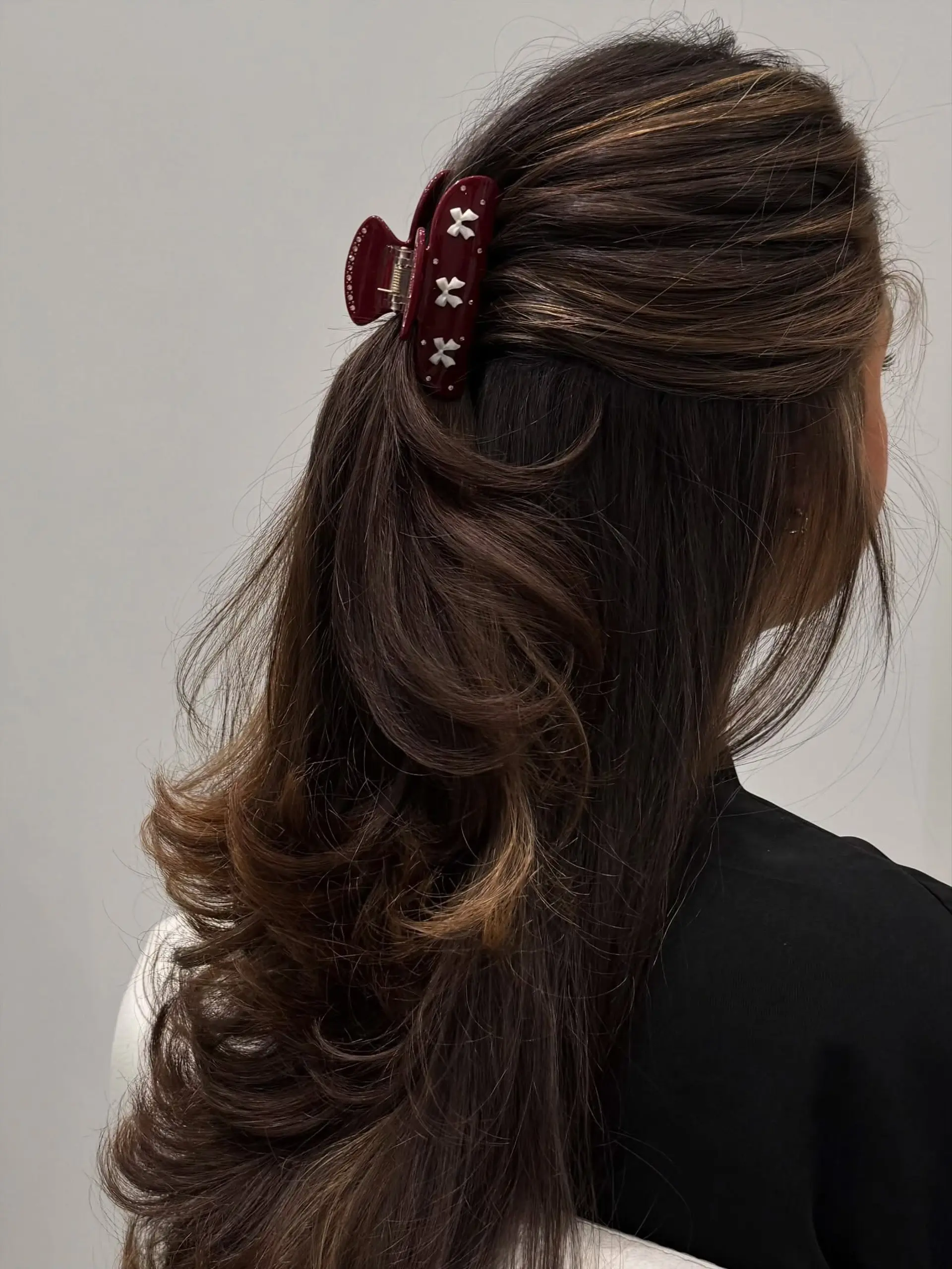 Long dimensional brunette hair cut with soft cascading layers, styled in a voluminous blowout and clipped in a half-up style. 1