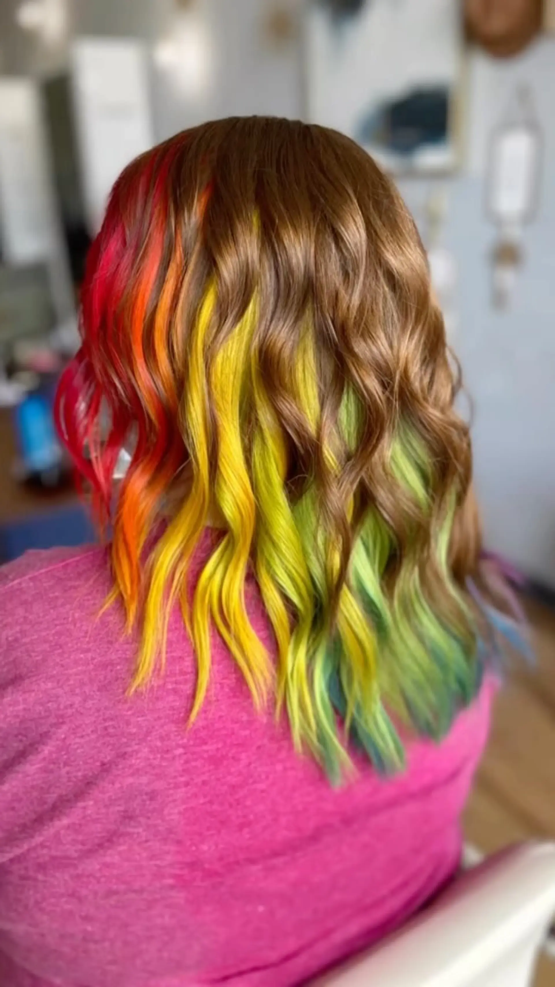 Medium-length light brown hair styled in soft textured waves with vivid rainbow peekaboo underlights. 1