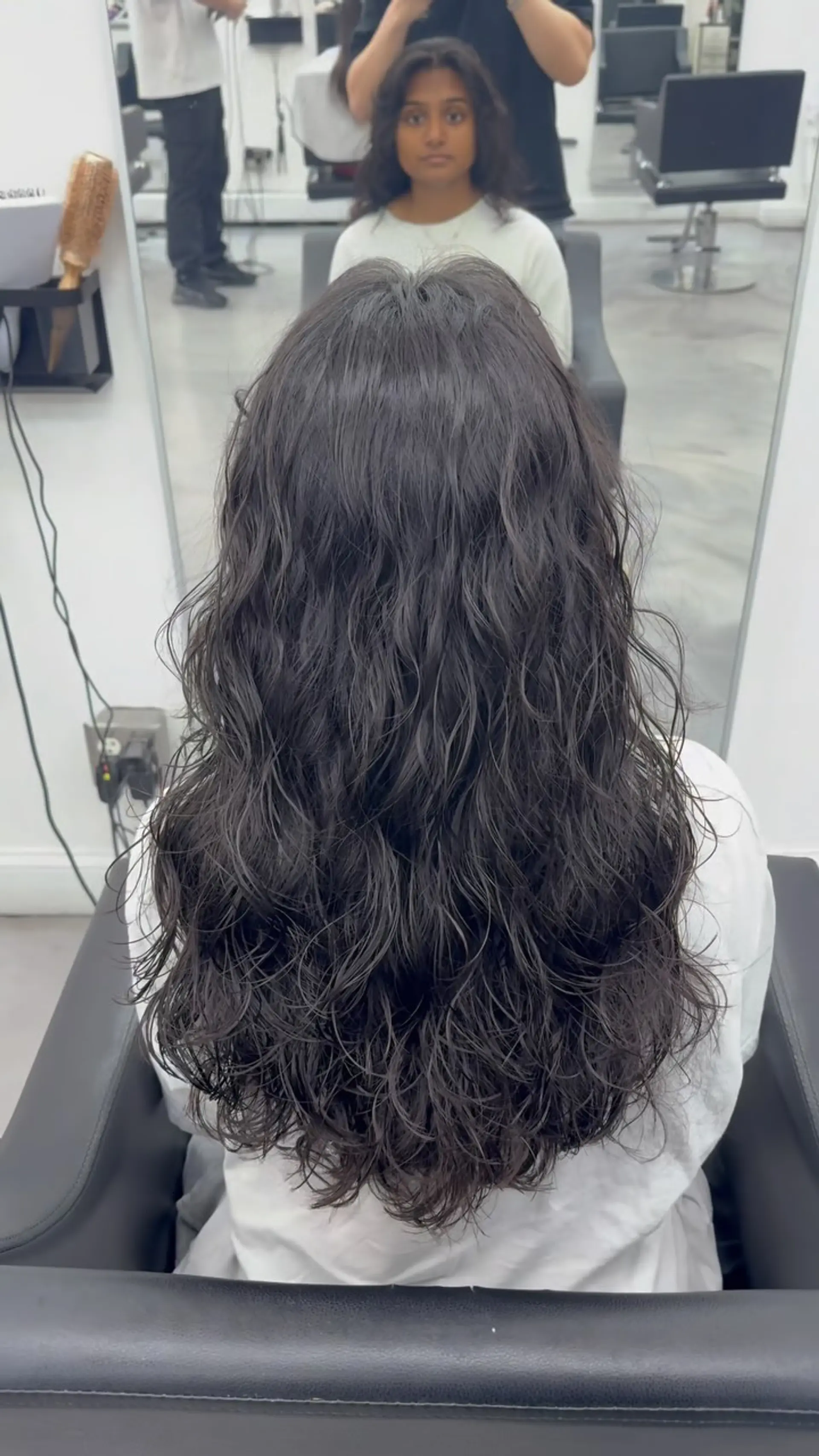 Long dark hair styled into soft, tousled French perm waves with natural texture and airy definition. 1