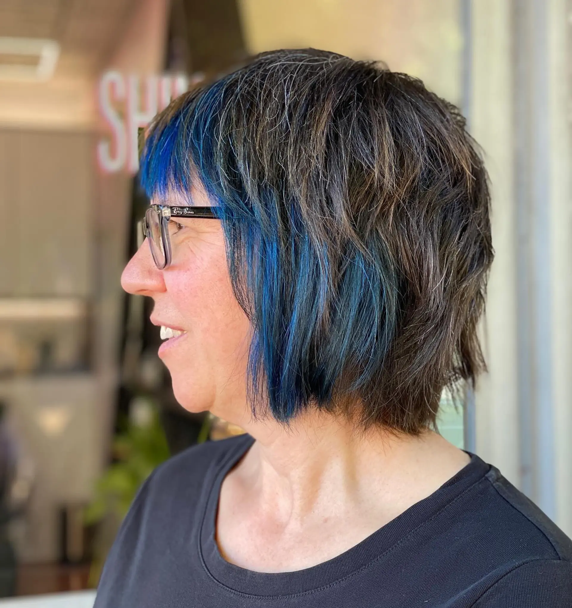 A textured shaggy bob featuring choppy layers, straight-across fringe, and a striking vivid blue face-framing panel. 1
